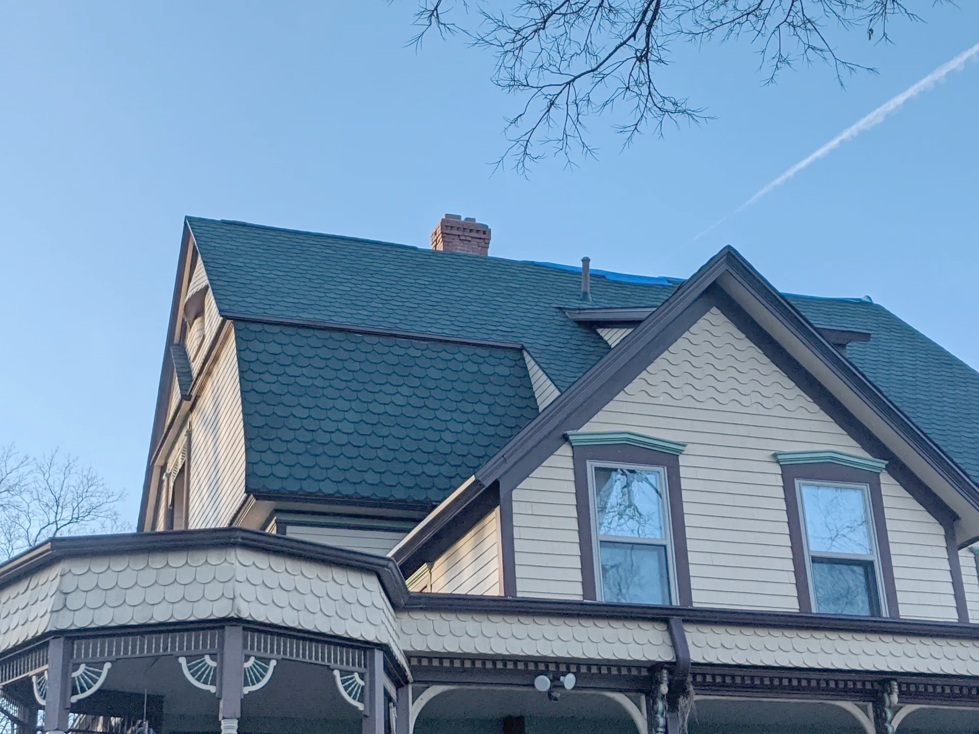 Victorian house with dark green roof and chimney under a blue sky, some bare tree branches.