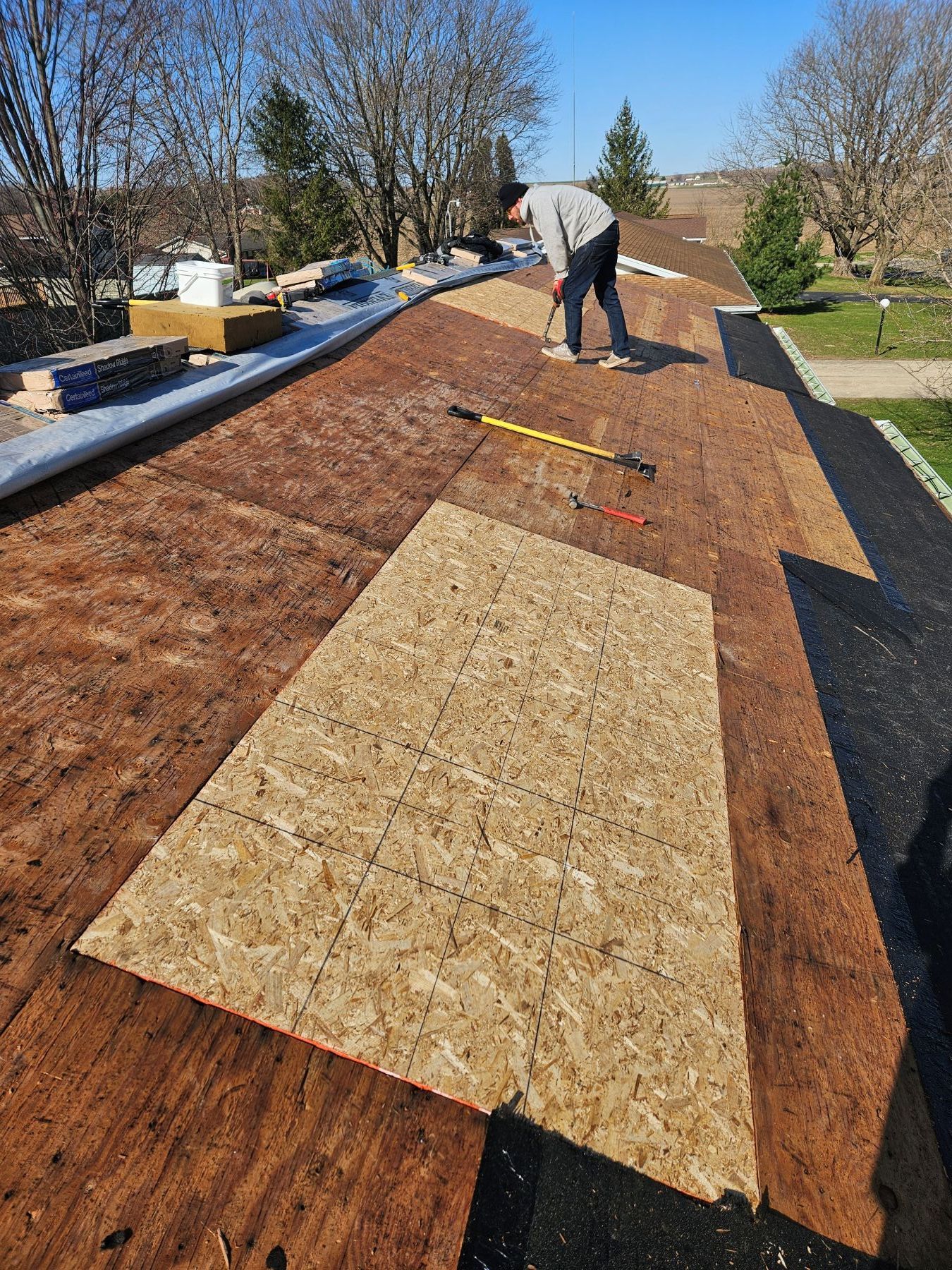 Person on a roof working with wood. Brown roof, blue sky.