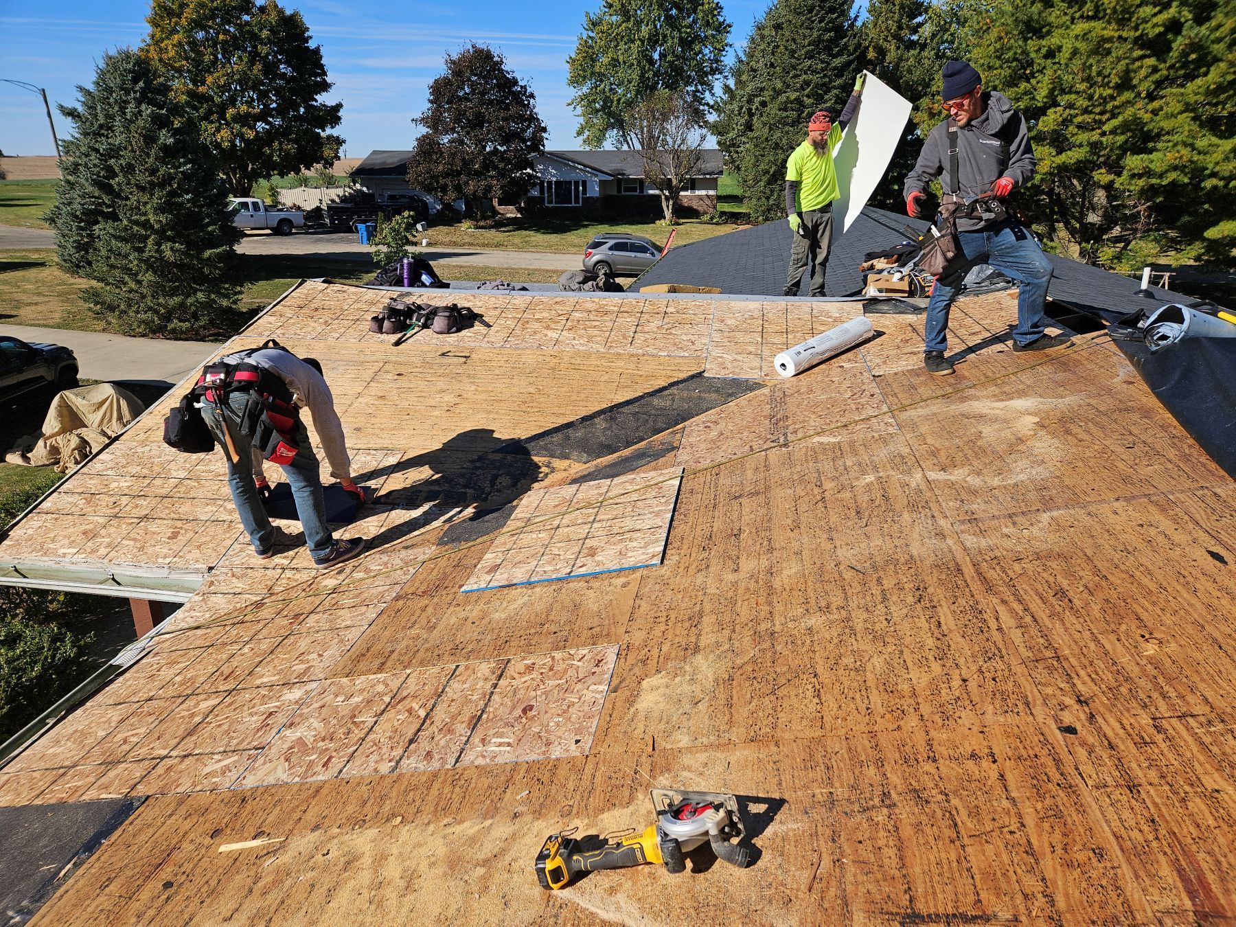 Roofers working on a residential roof, wearing safety gear.  Daytime, outdoors, sunny.