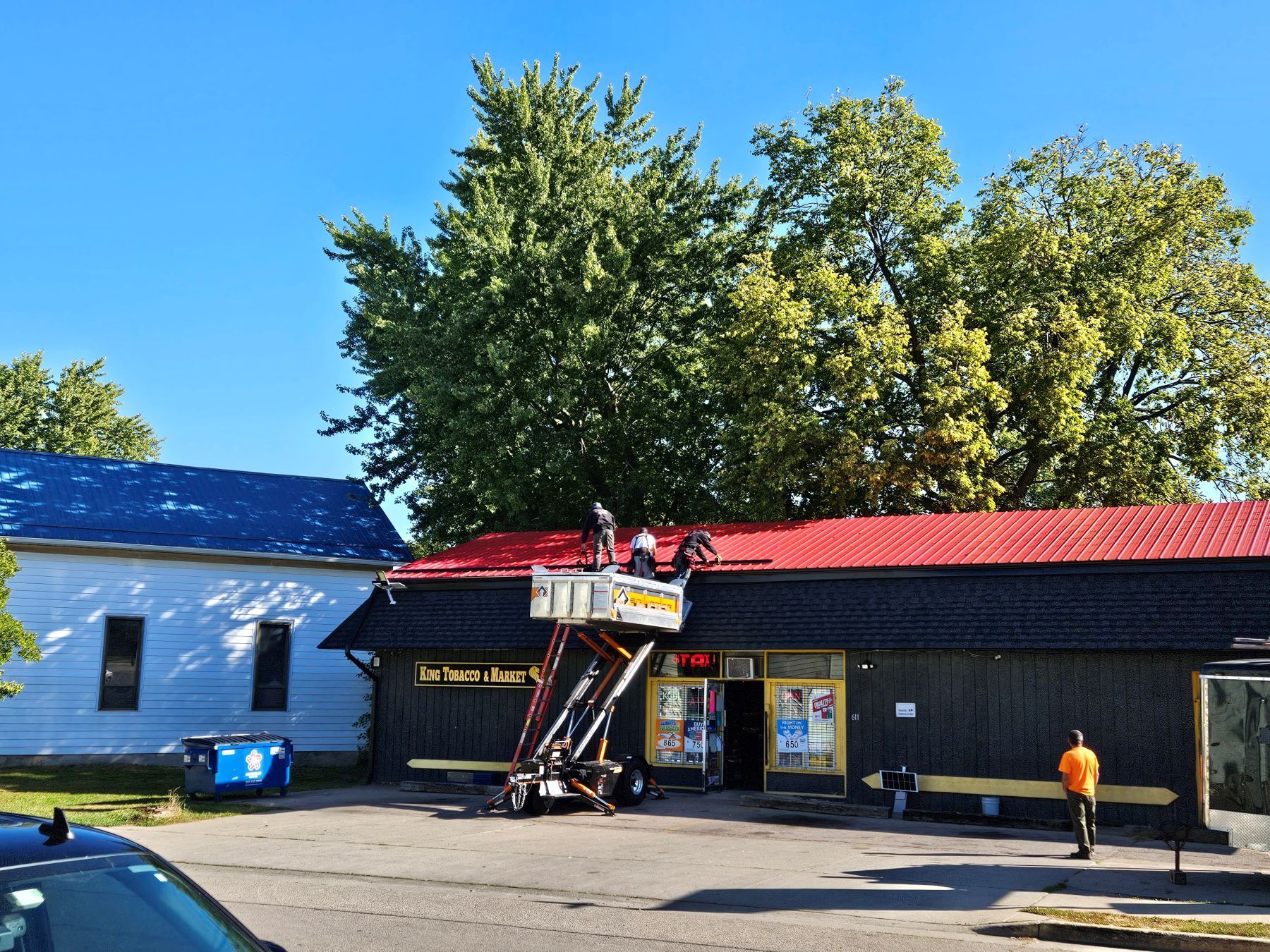 Workers on a lift repairing the red roof of a black building, sunny day.
