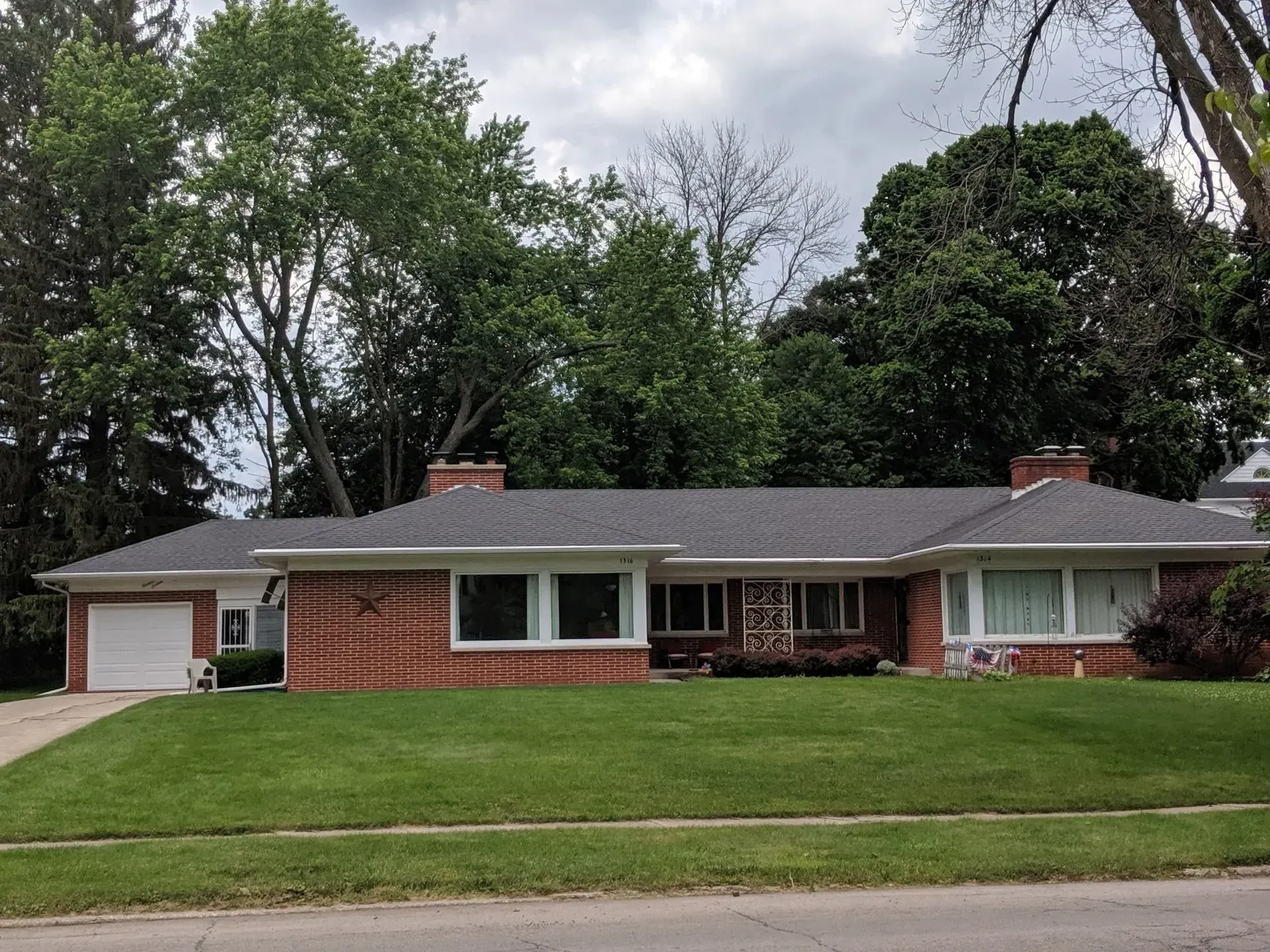 Low-slung brick ranch home with a garage, windows, and a green lawn. Trees in the background.