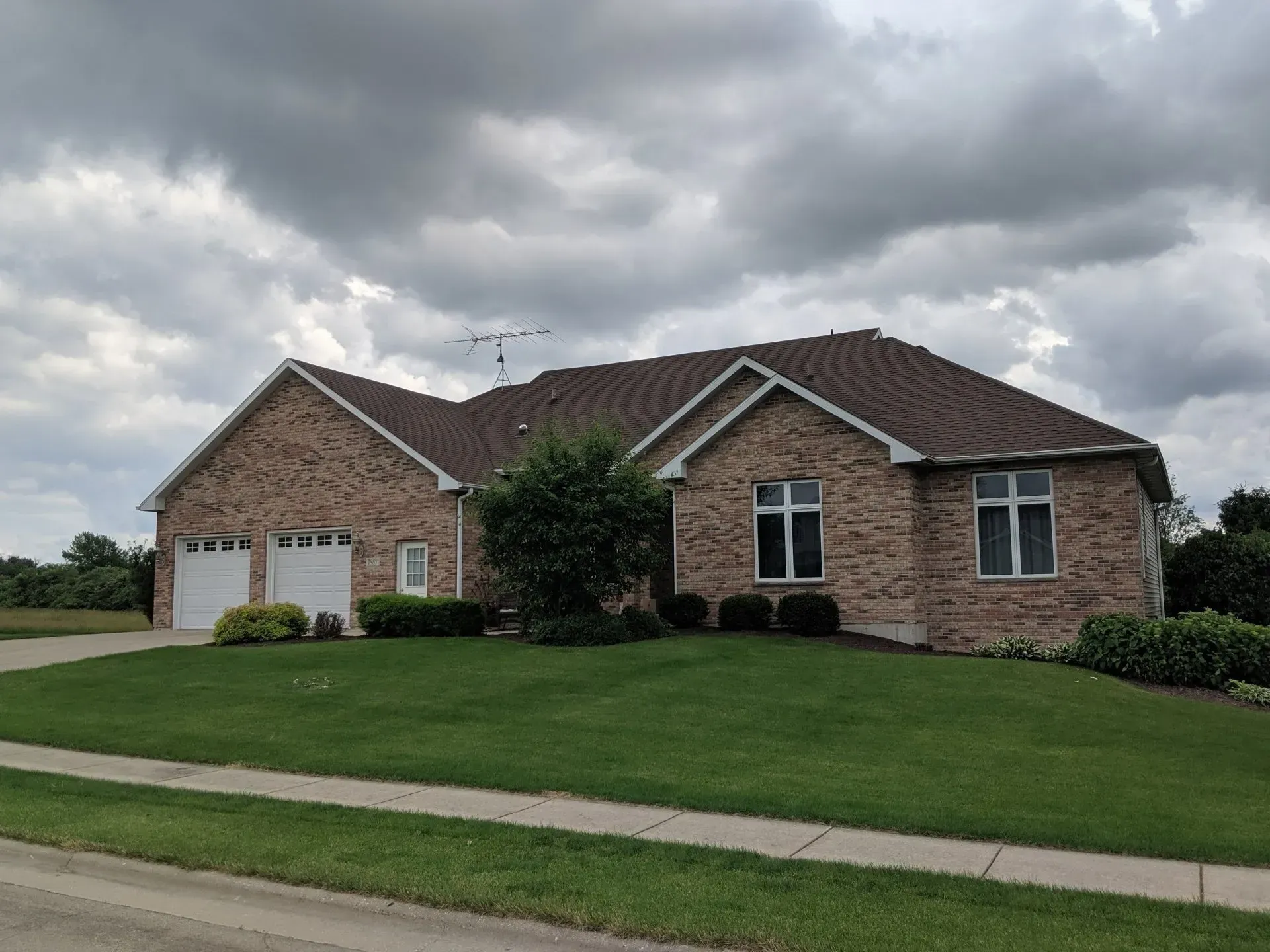 Brick house with a two-car garage, windows, and a brown roof, under a cloudy sky.