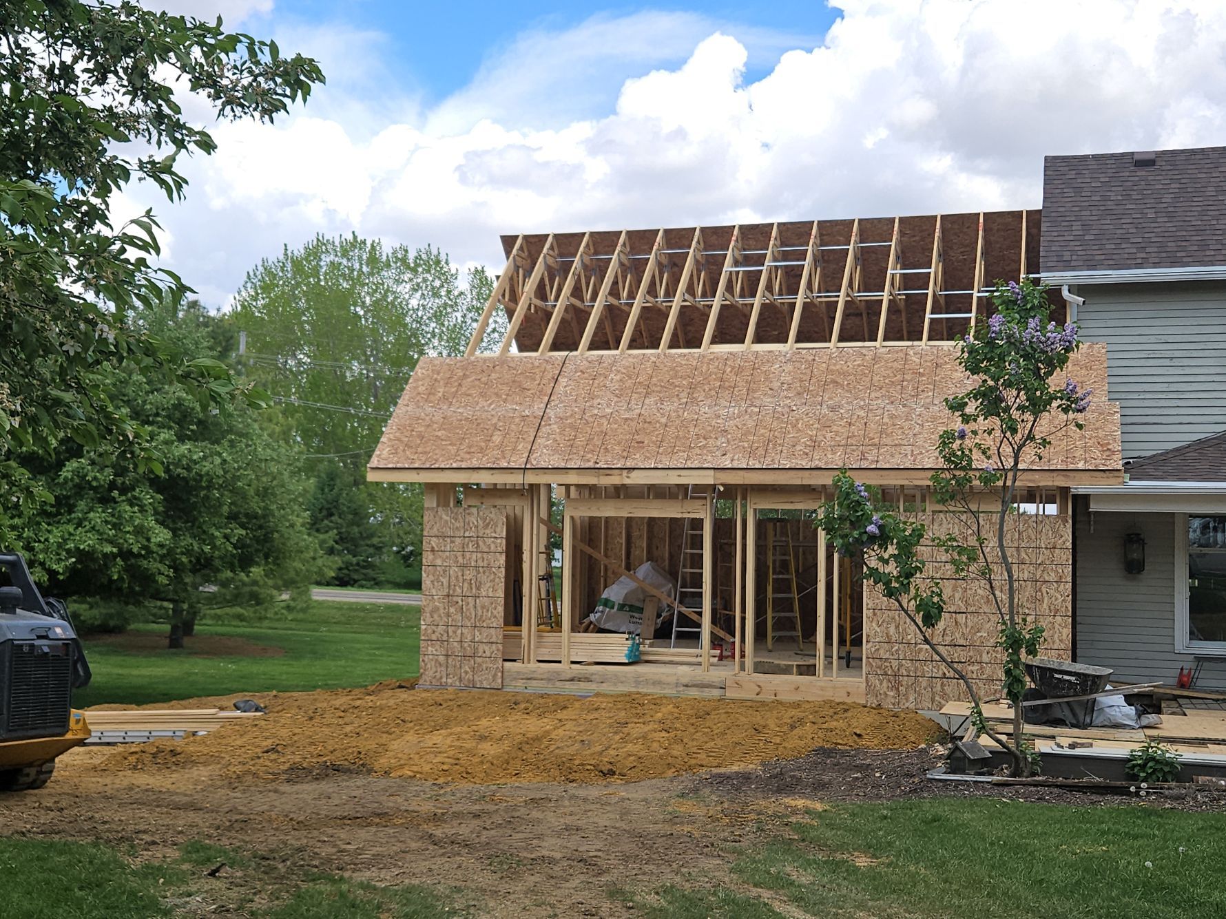 Construction of a small shed-like structure next to a house, brown siding, wooden frame, outdoor setting.