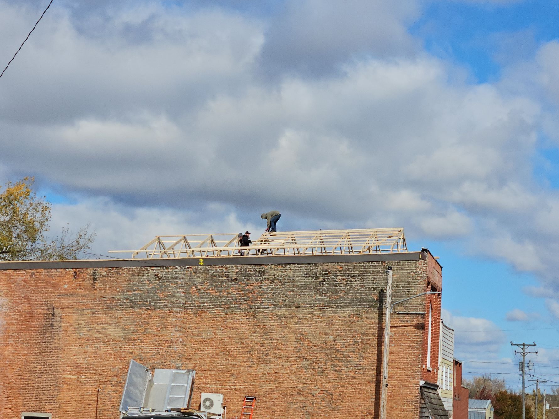 Two construction workers on a brick building's roof under a cloudy sky, building a framework.