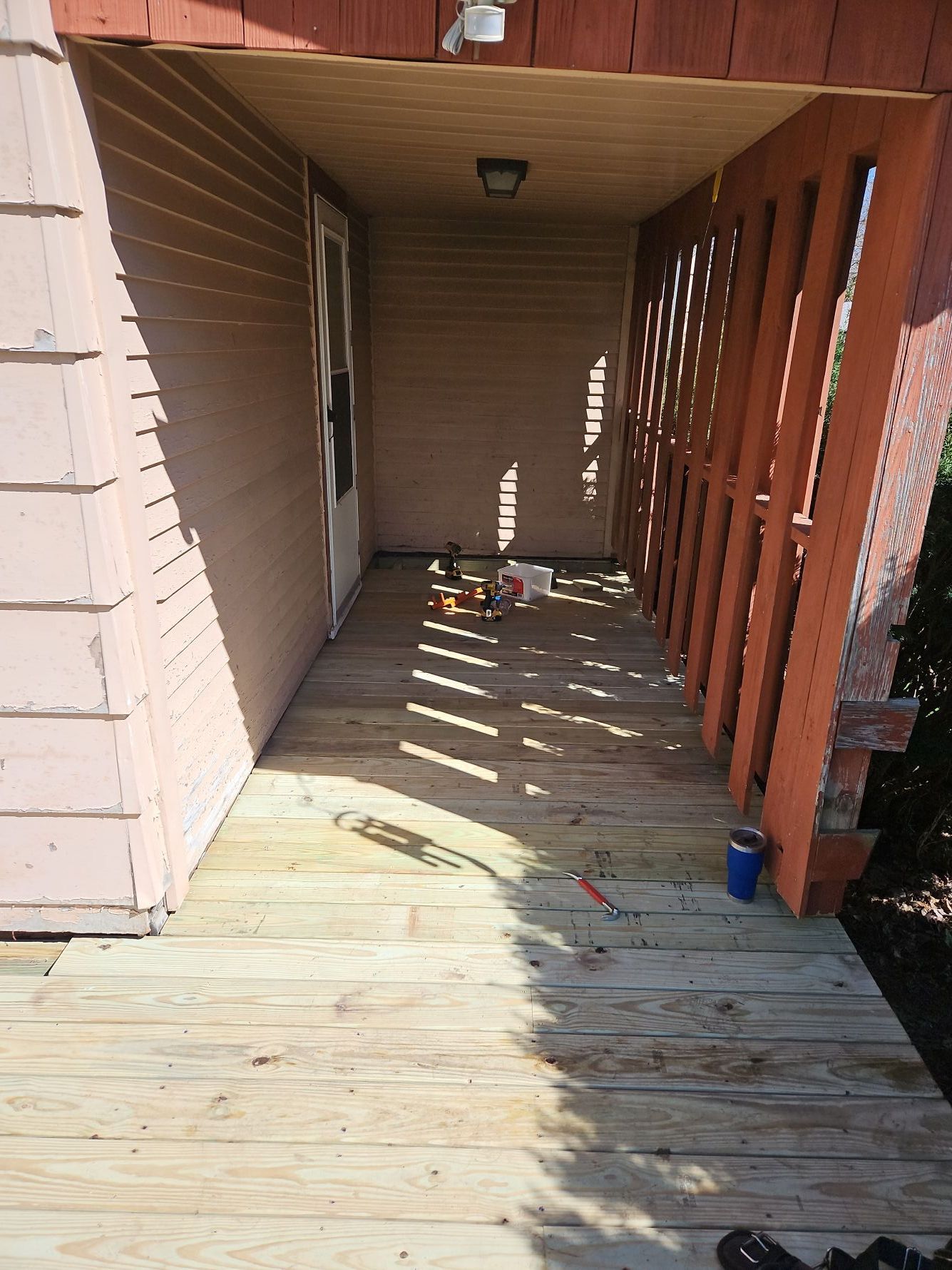 Wooden porch with doorway. Brown siding and railing. Tools visible.