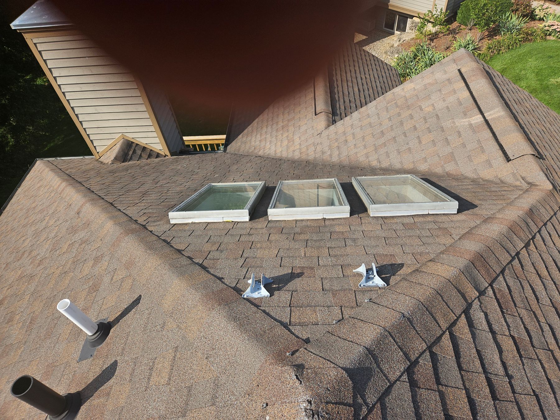 Overhead view of a shingled roof with three skylights, metal flashing, and a chimney pipe.