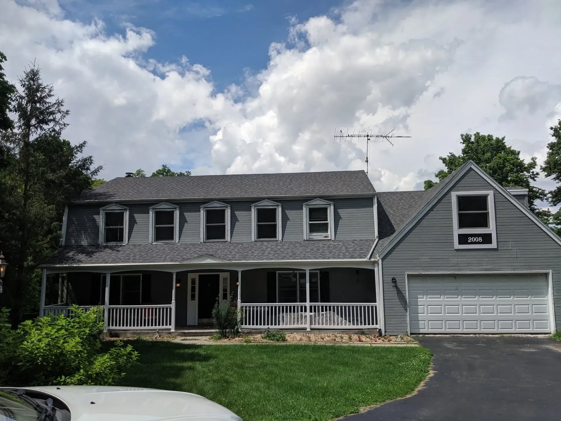 Gray house with a porch, dormer windows, a two-car garage, and a blue sky with clouds.