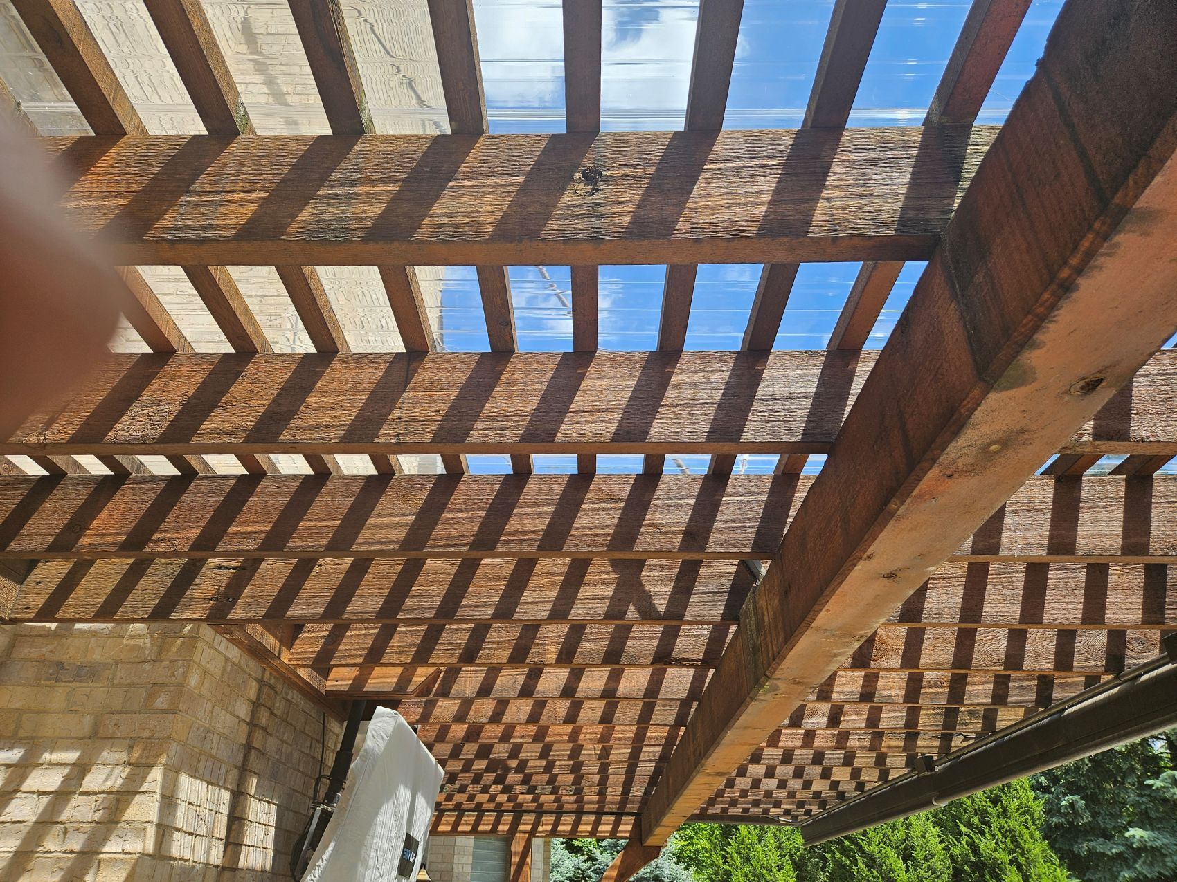 Wooden pergola with alternating shadows and sunlight cast on a structure with partial clear panels.