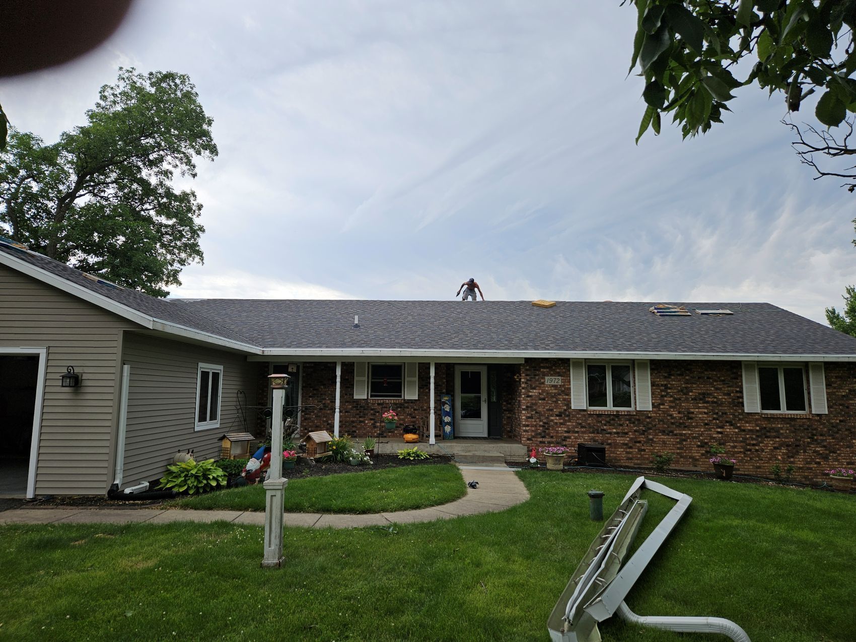 House with a partially replaced dark roof; a person stands on the roof.