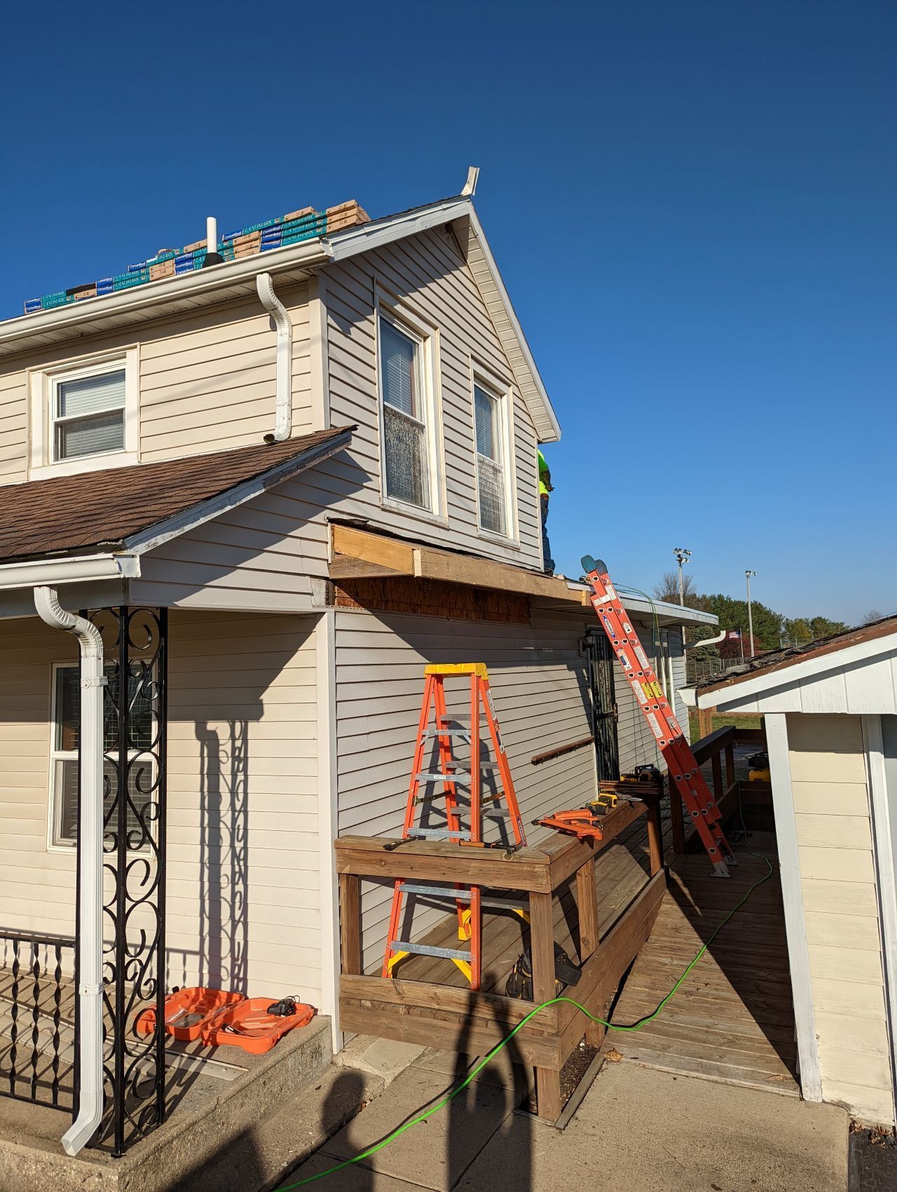 House under construction; siding partially removed, ladder against wall, tools on a deck, clear sky.