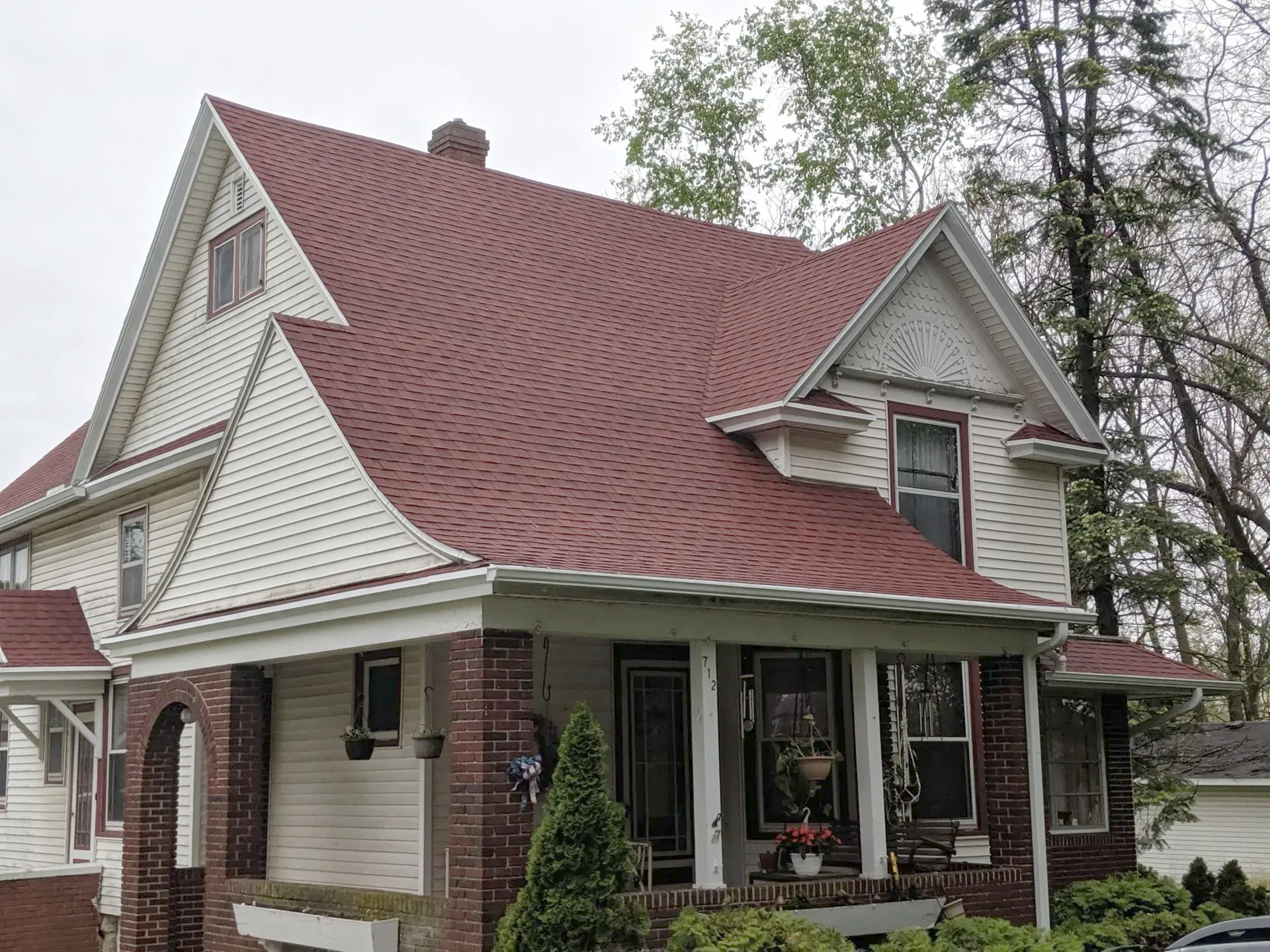 Two-story house with red roof, white siding, and porch, set against a cloudy sky.