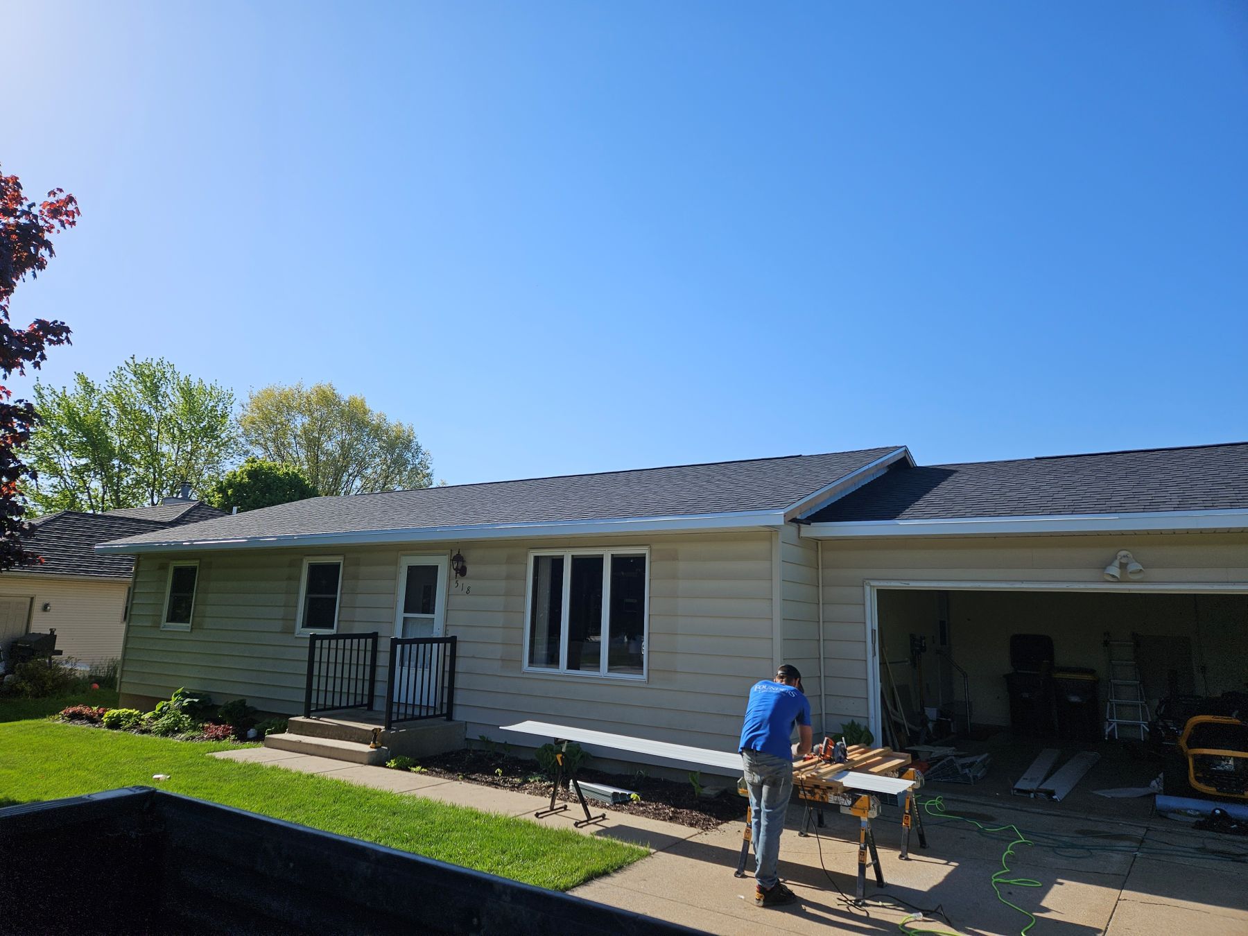 A man working on the roof of a one-story beige house on a sunny day.