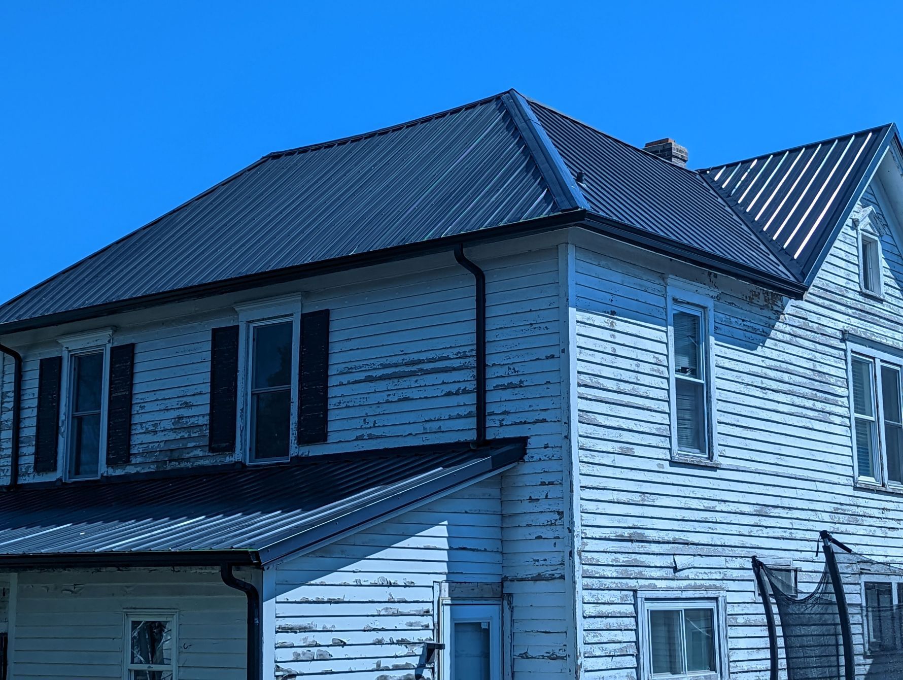 Two-story white house with a dark metal roof under a blue sky.