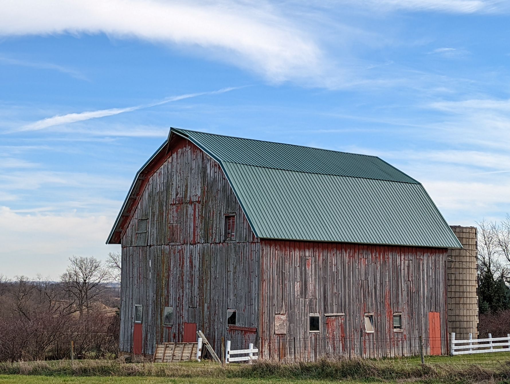 Weathered red barn with green roof, against a blue sky with faint clouds.