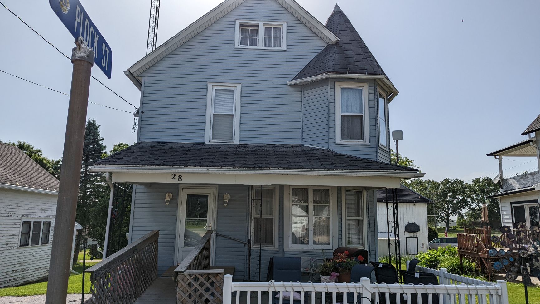 Blue two-story house with a small turret, porch, and street sign on a sunny day.