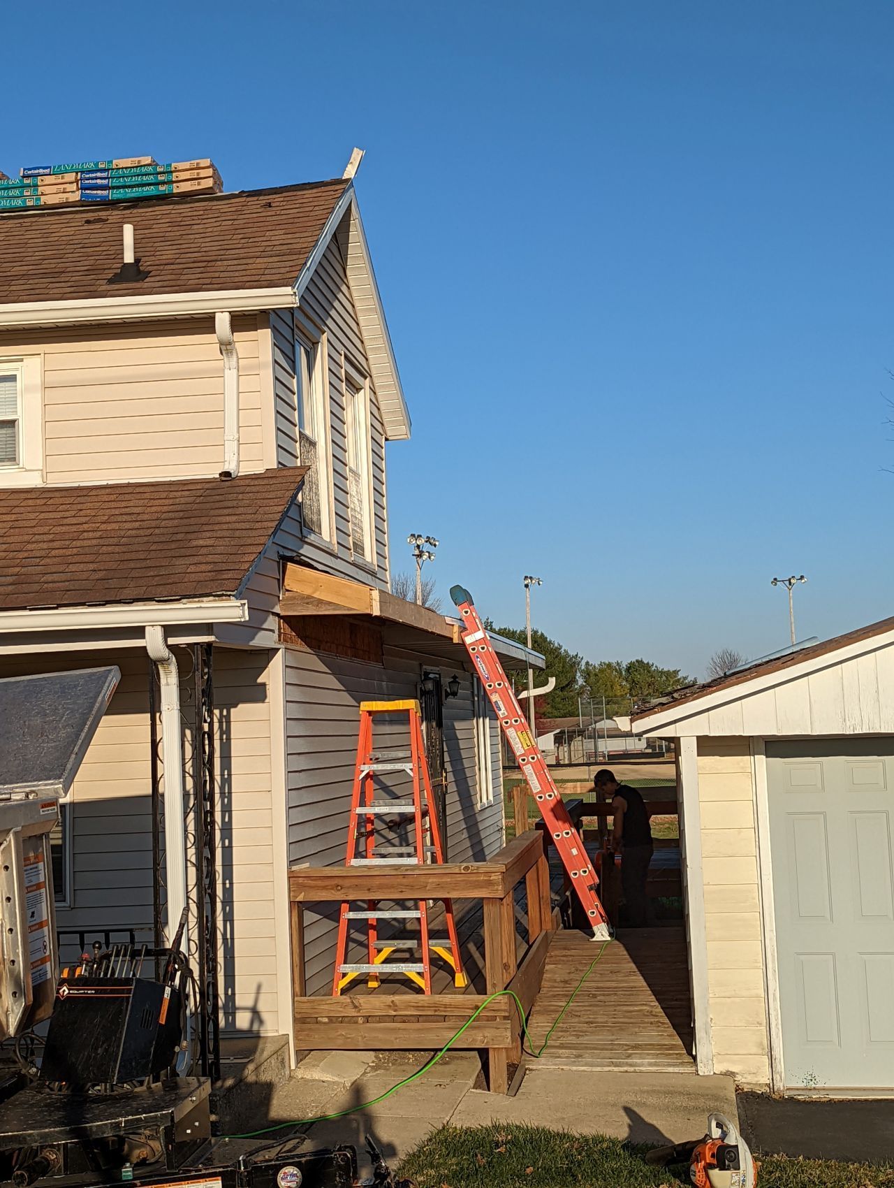 A house with a roof being worked on, orange ladder propped up, wooden deck.