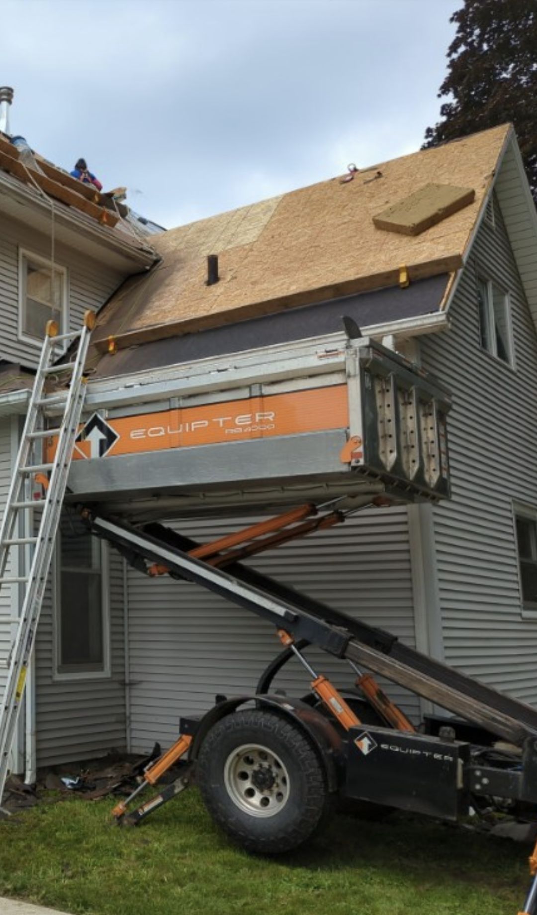 Roofers working on a house roof, using a debris removal lift. The lift is orange and silver.