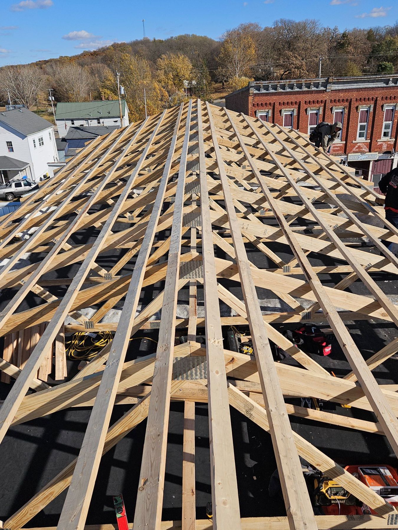 Roof under construction with wooden beams and support structure. Workers are on the roof on a sunny day.