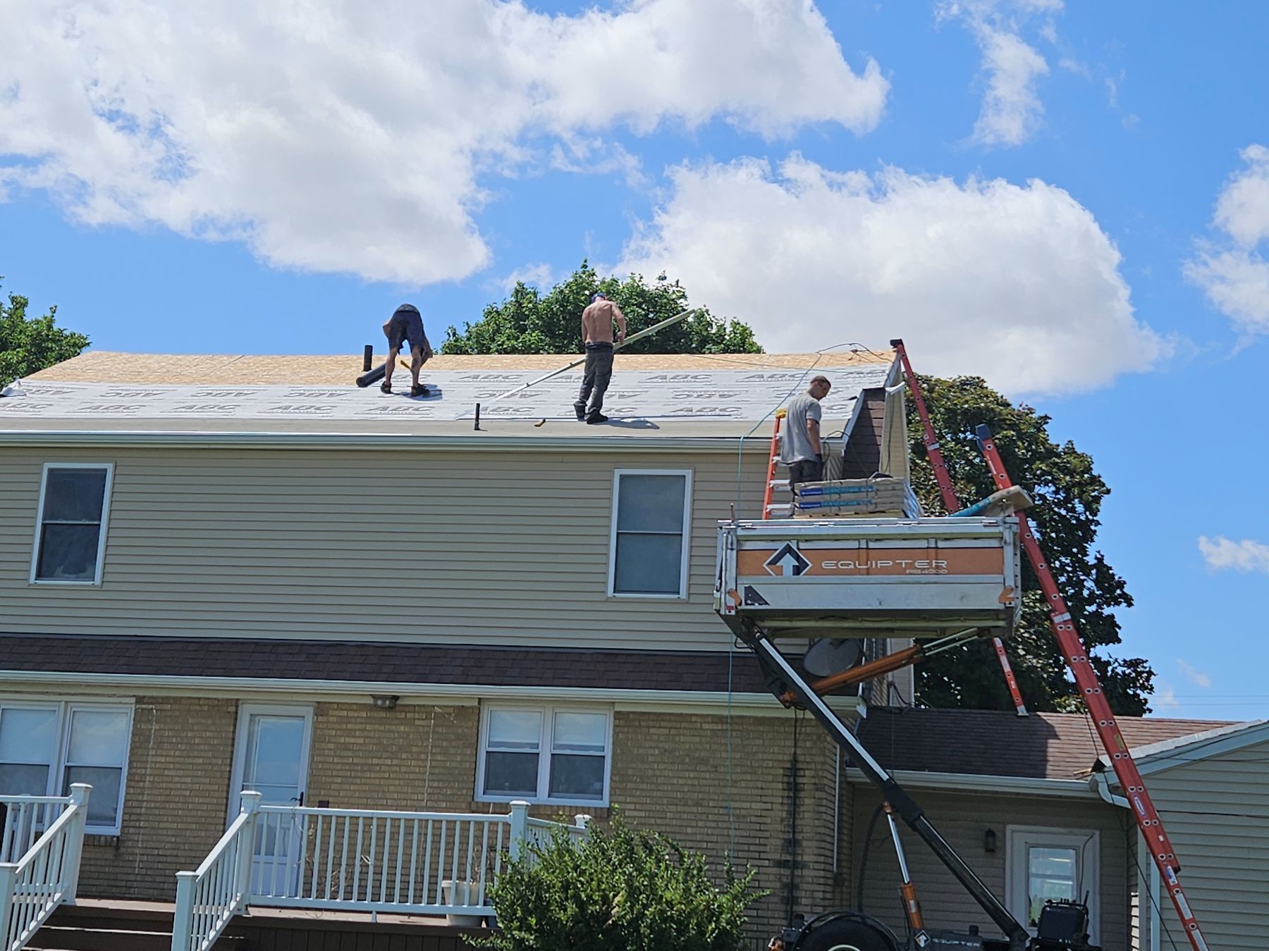 Roofers working on a house under a partly cloudy sky, using a lift.