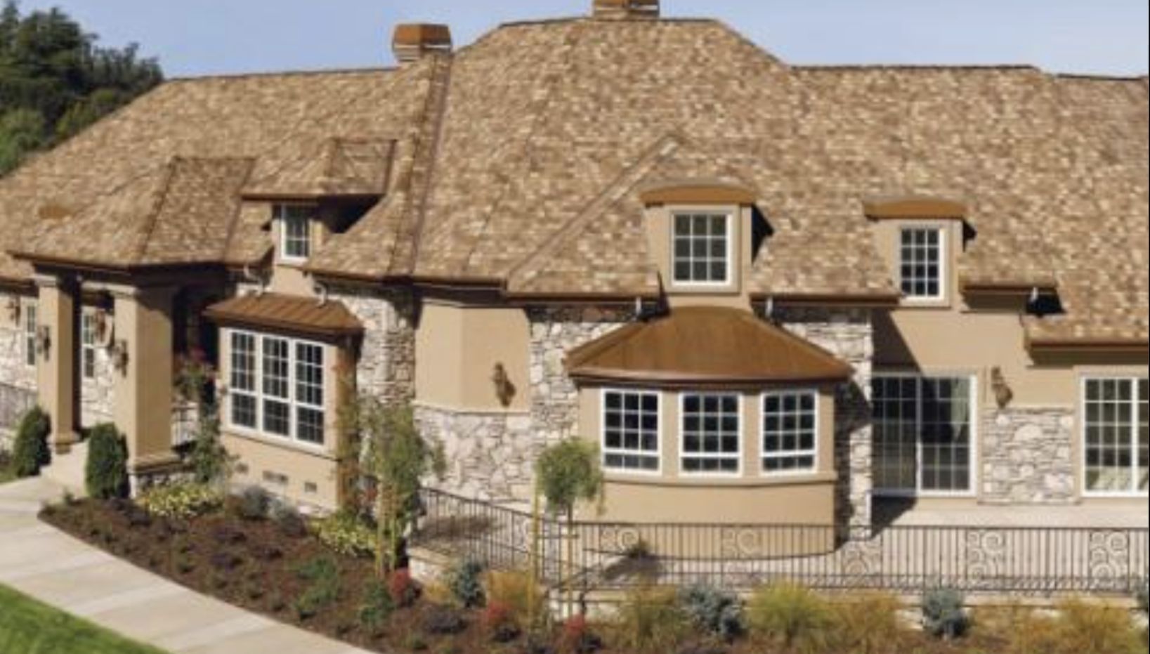 Beige stucco house with stone accents, brown roof, and white-framed windows. Landscaping in front.