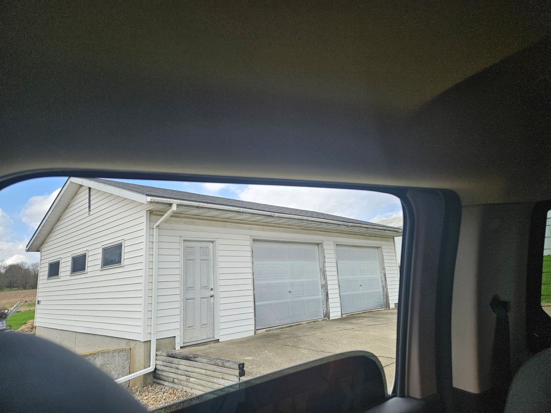 White garage with three bay doors viewed through a car window on a sunny day.