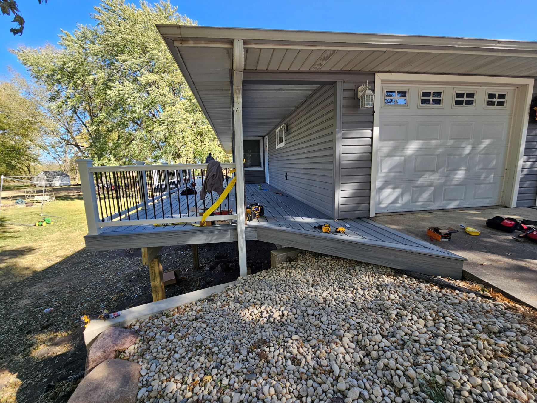 Grey house with a porch and ramp, next to gravel.