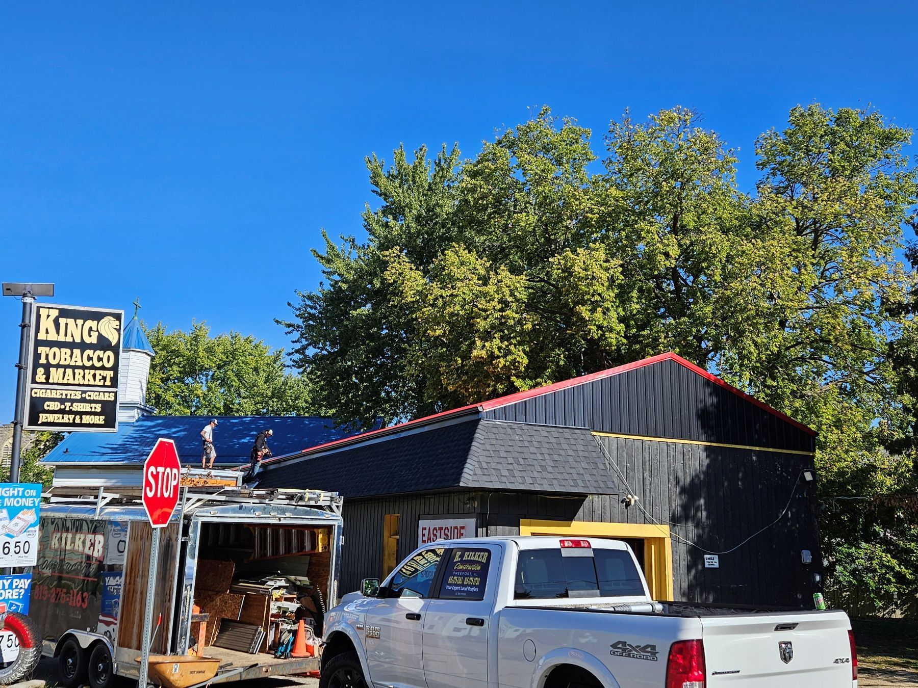A tobacco and bullet shop with a trailer, pickup truck, and a stop sign on a sunny day.