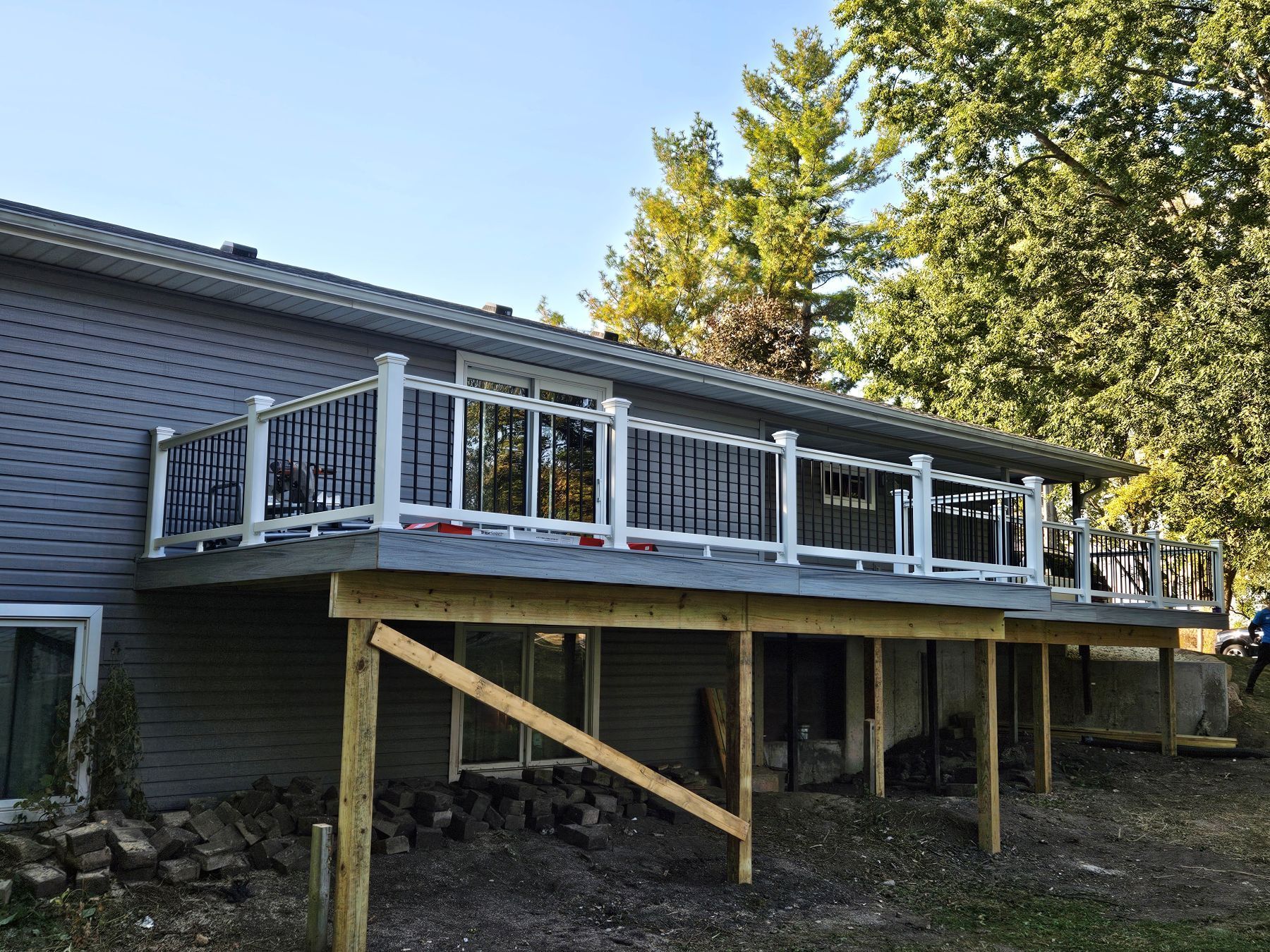 Newly constructed deck with white and black railings attached to a gray house, supported by wooden posts.