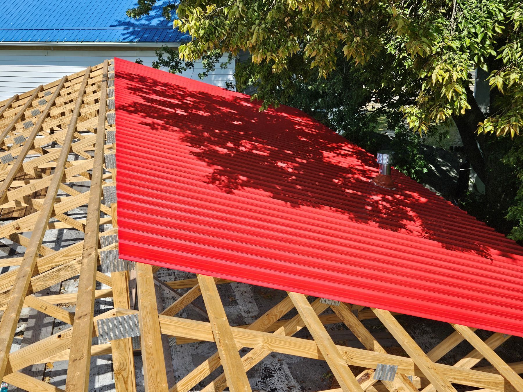 Red corrugated metal roof being installed on wooden rafters.