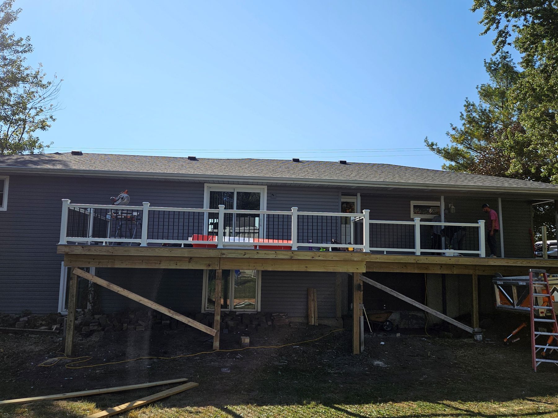 A partially built wooden deck attached to a gray house, with white railings and support beams.