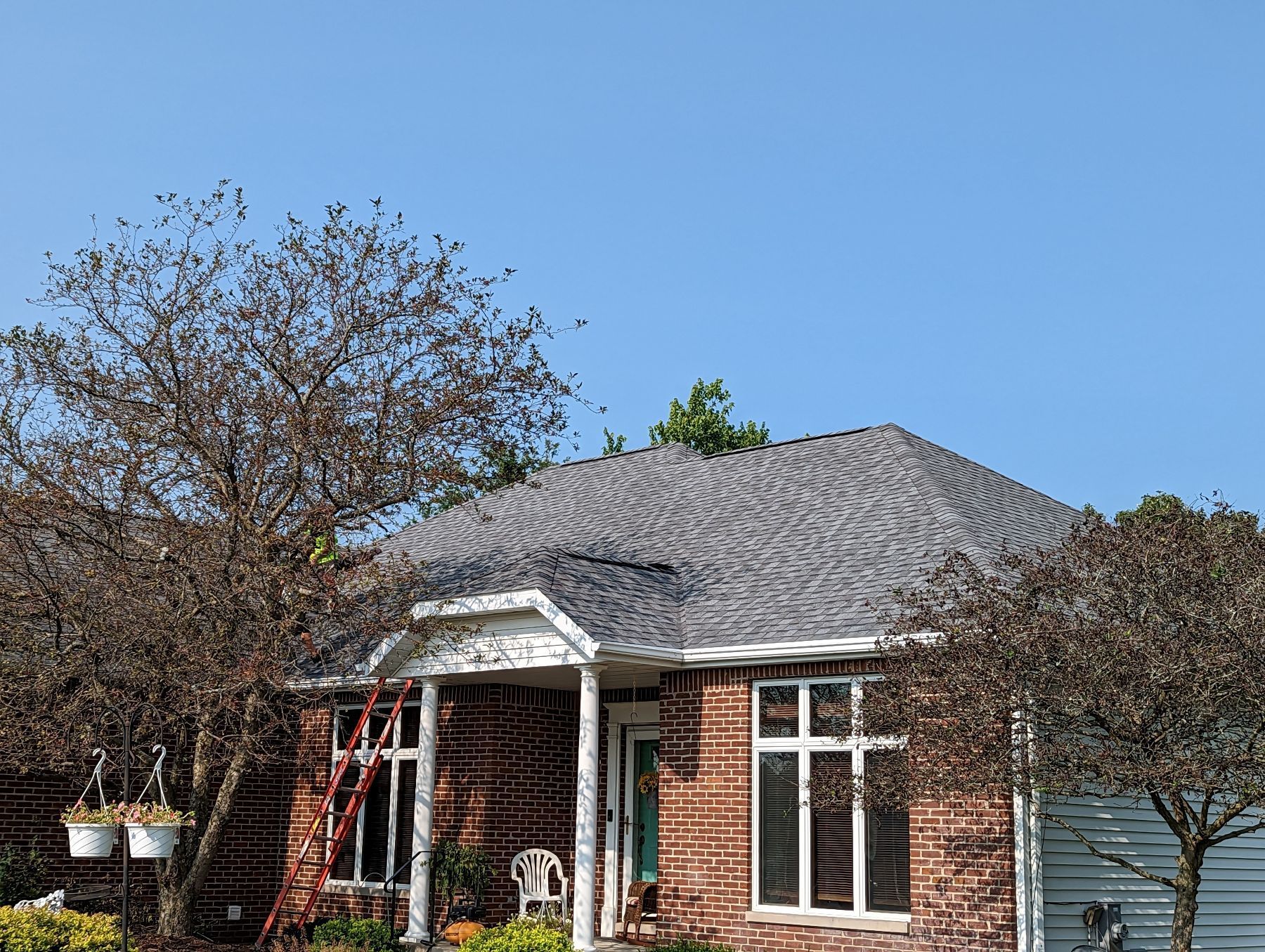 Brick house with a gray shingle roof, surrounded by trees. Blue sky overhead.