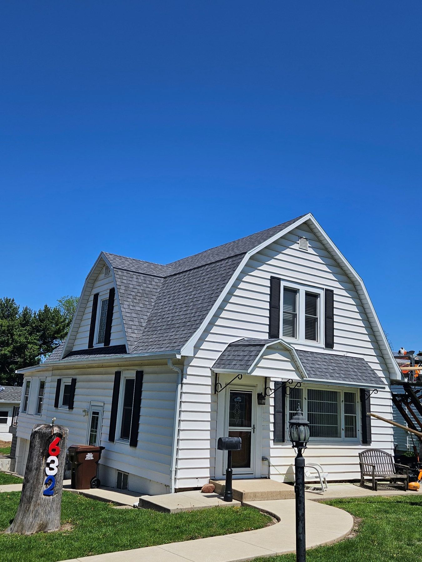 White house with dark shutters, front porch, and blue sky. House number on a post.