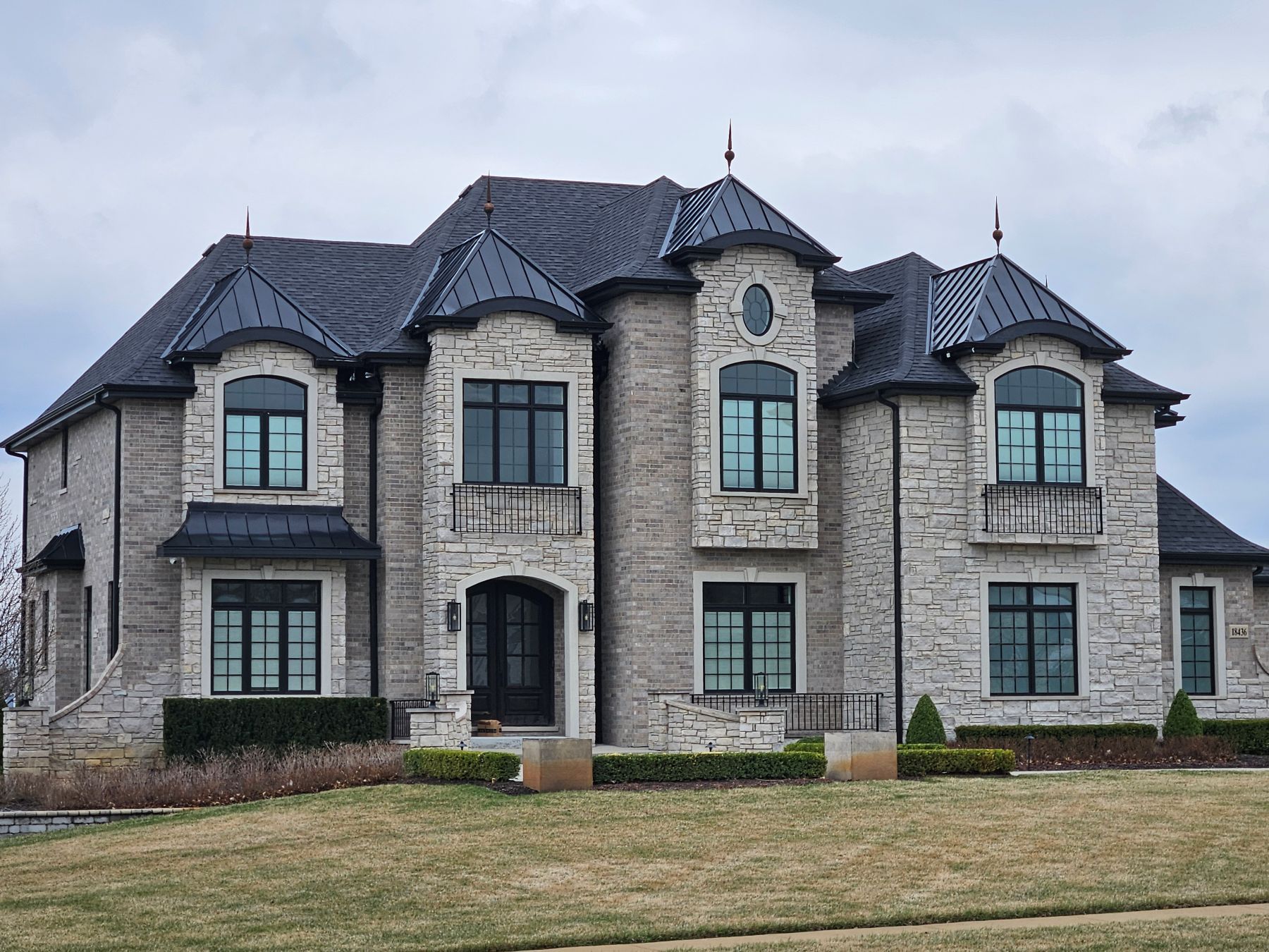 Large stone house with black-framed windows and dark roof, set on a lawn with sparse grass.