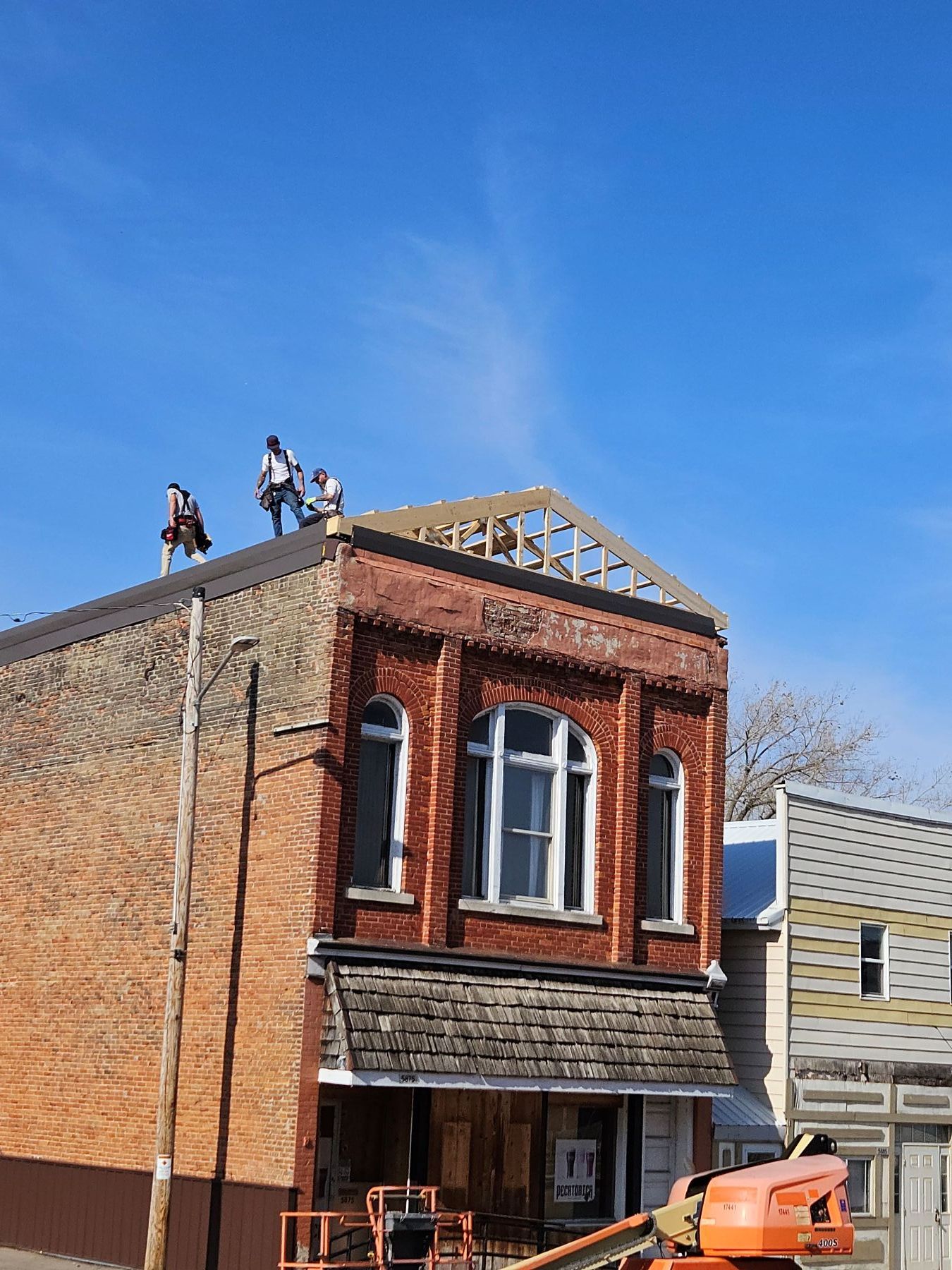 Construction workers on a brick building's roof with wooden framework, under a blue sky.