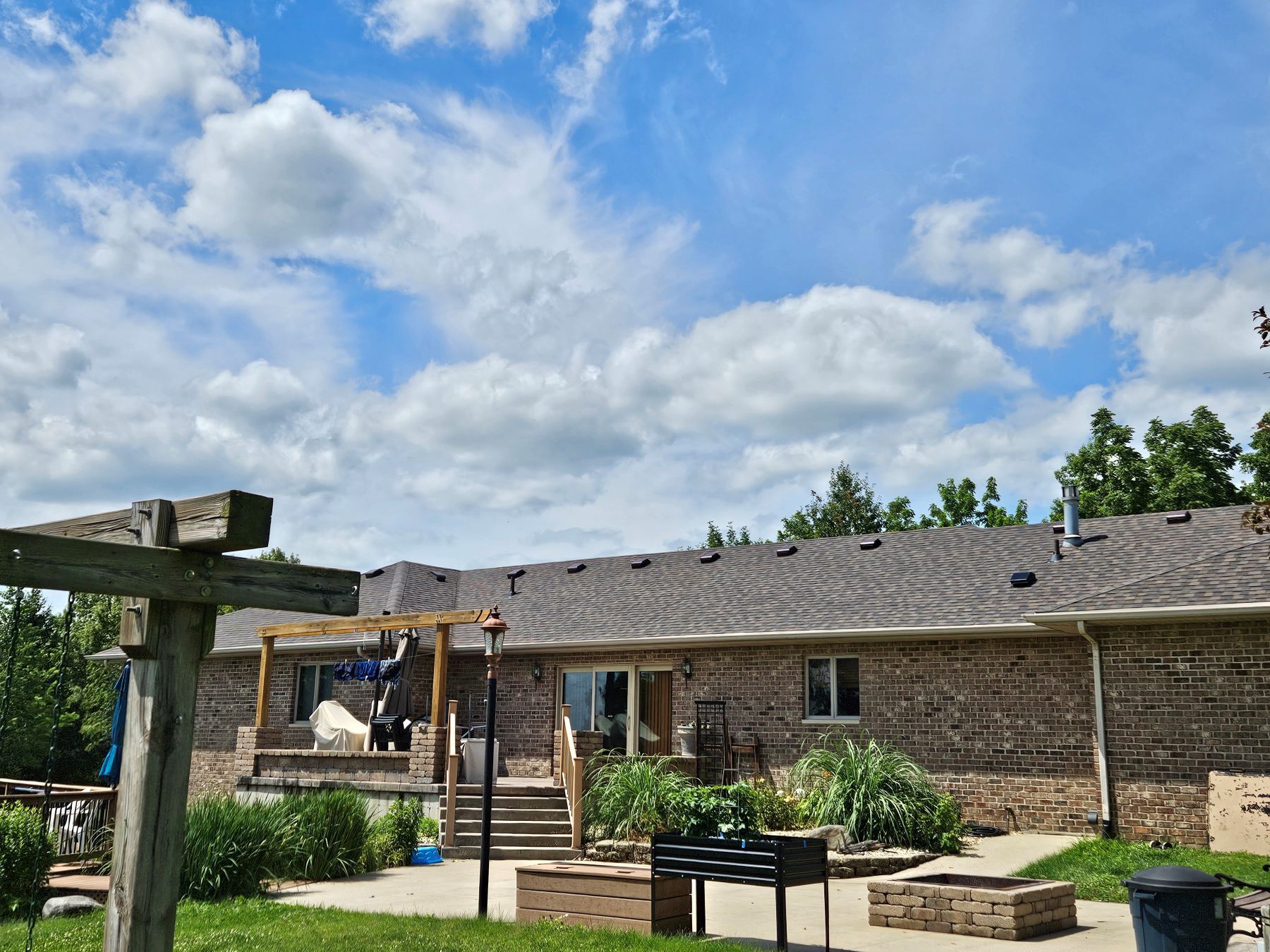 A brick house with a wooden pergola in front, under a blue cloudy sky.