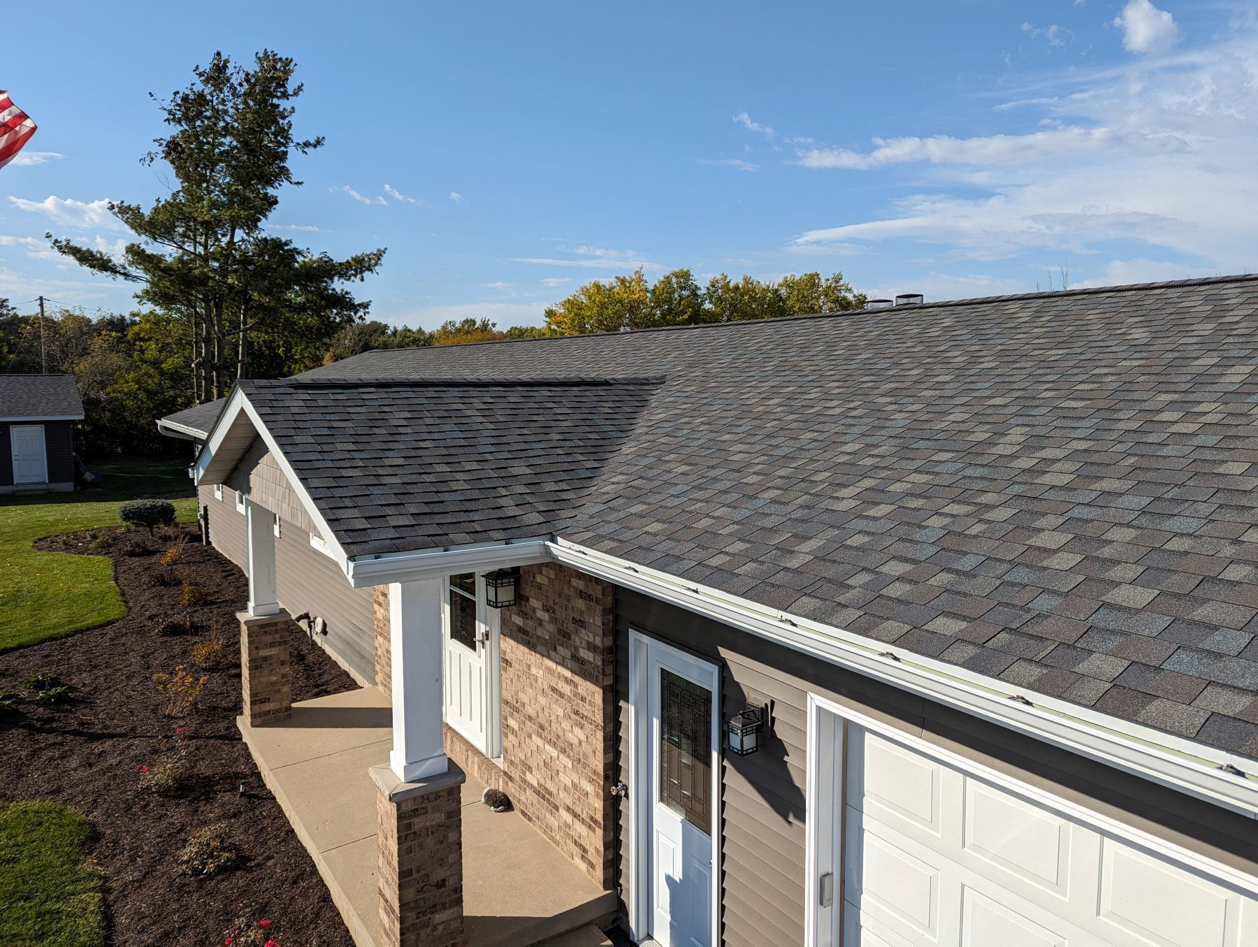 Low-angle view of a house with a dark gray shingle roof, white trim, and a small front porch on a sunny day.