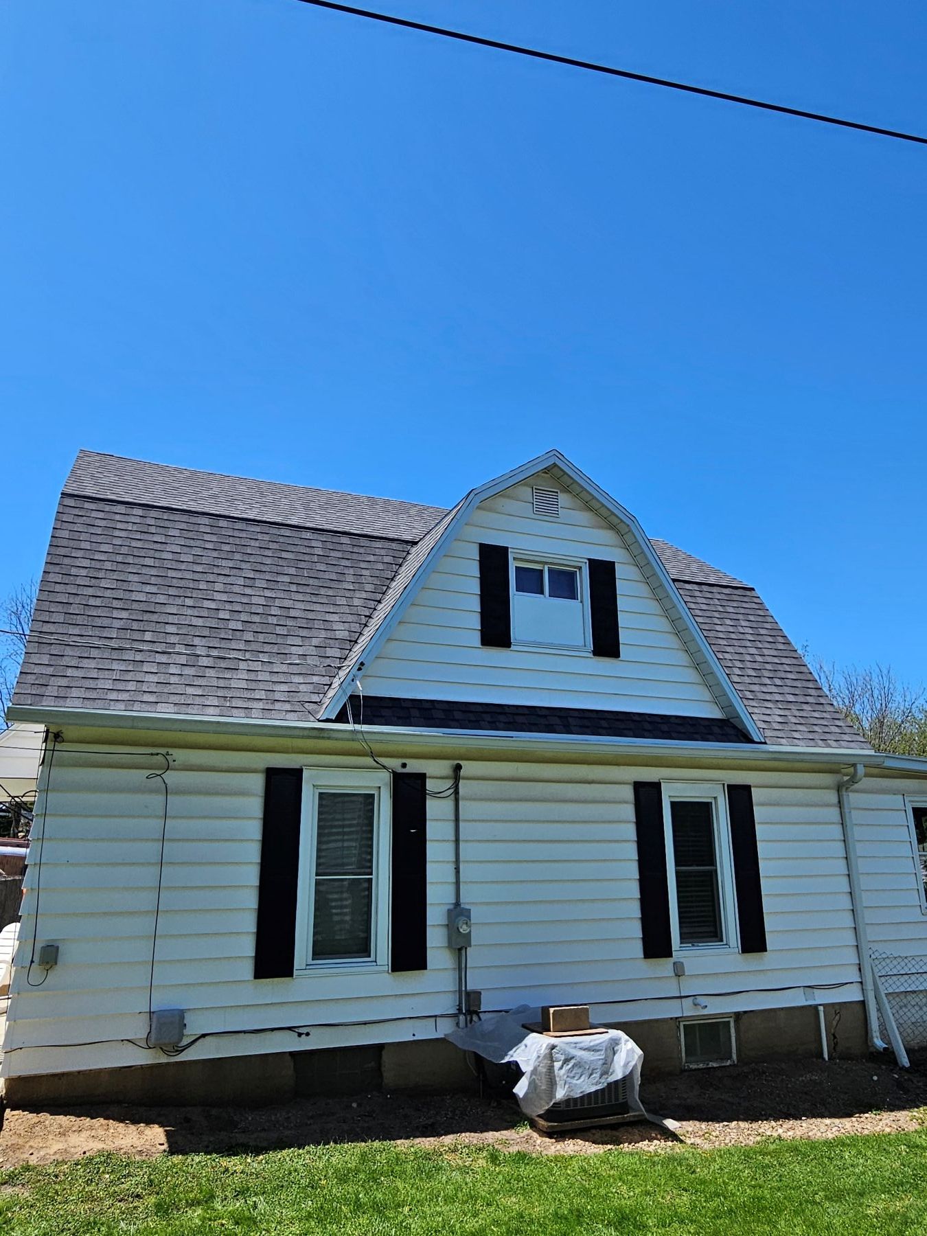 White house with a gray roof and black shutters under a clear blue sky.