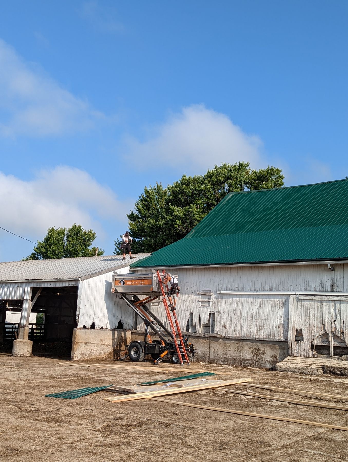 Barn with green roof, lift, and materials, under blue sky.