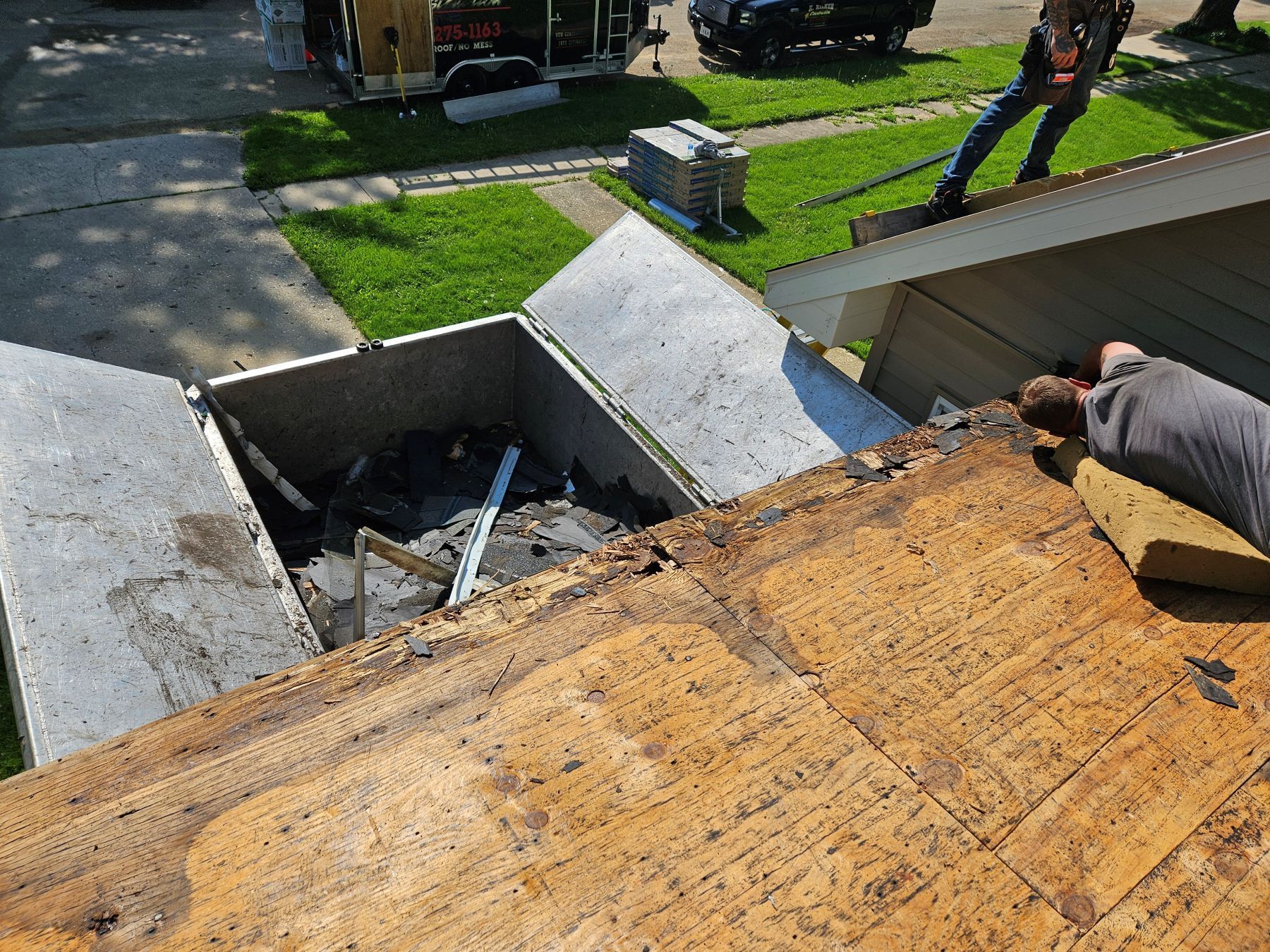 Roofers removing old shingles, debris in a container, asphalt shingles, sunlight.