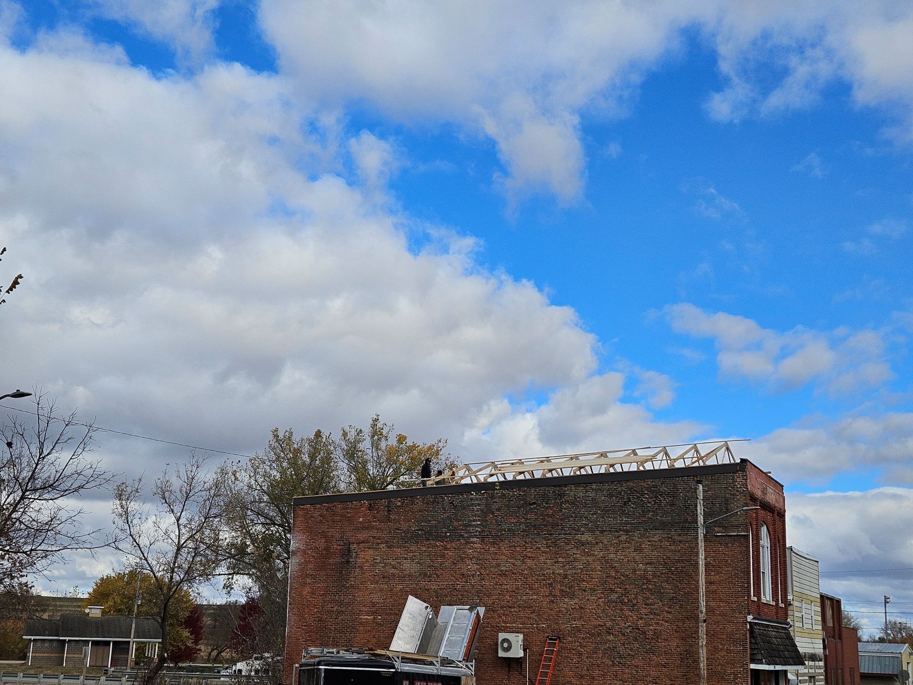 Brick building under a cloudy blue sky. Trees and utility poles in the background.