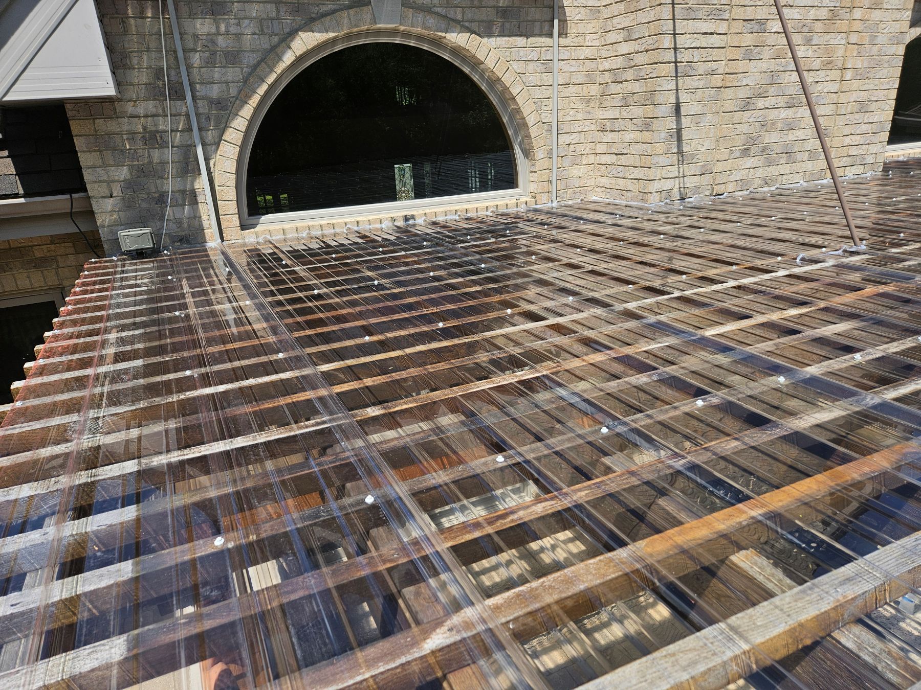 Clear corrugated roofing over wooden rafters, arched stone building in background.