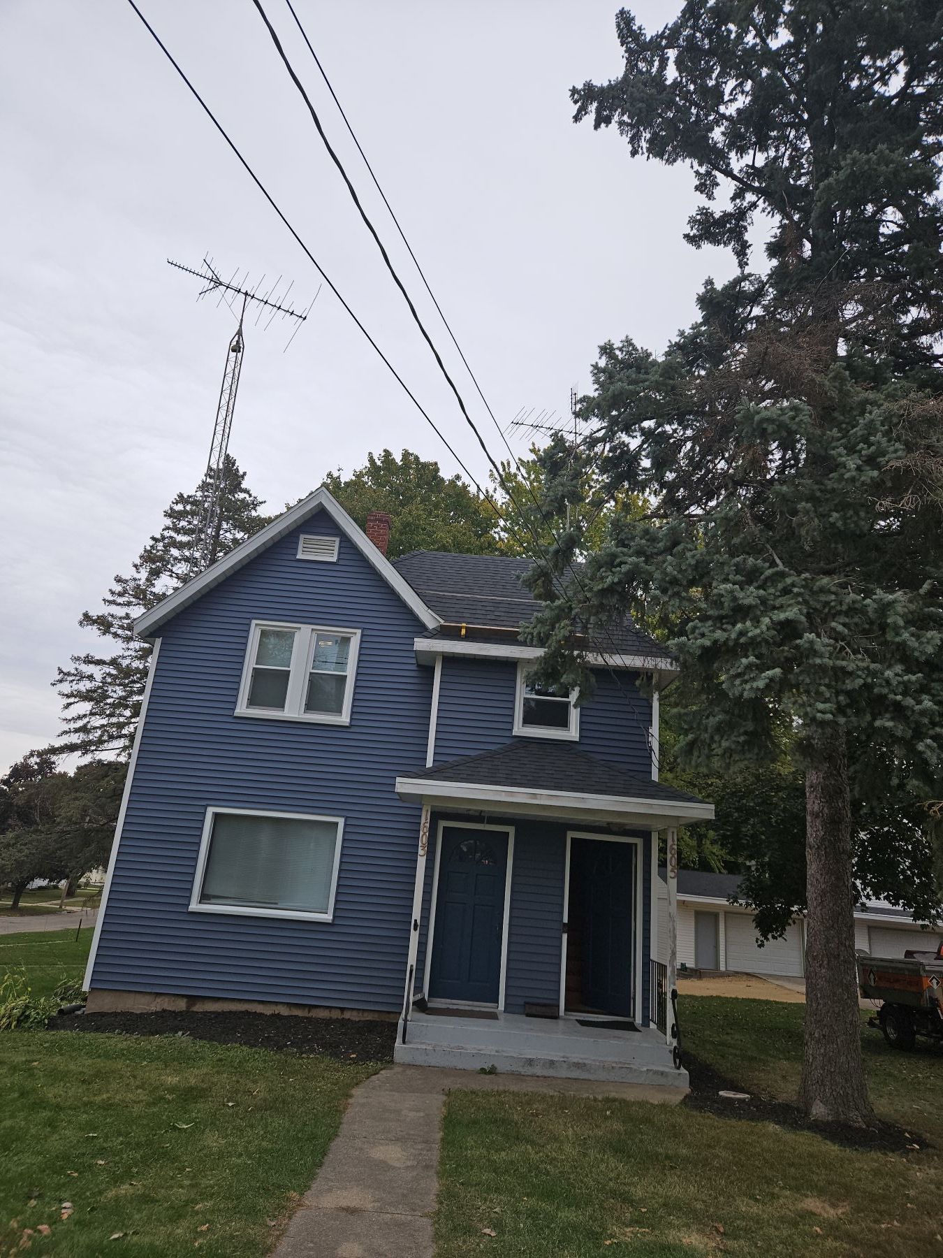 Blue two-story house with two front doors and a TV antenna; cloudy sky and trees.