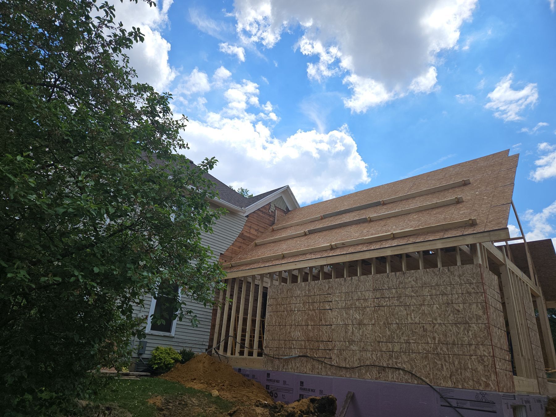 Construction of a new house addition. Wooden frame, OSB siding, under a blue sky with clouds.