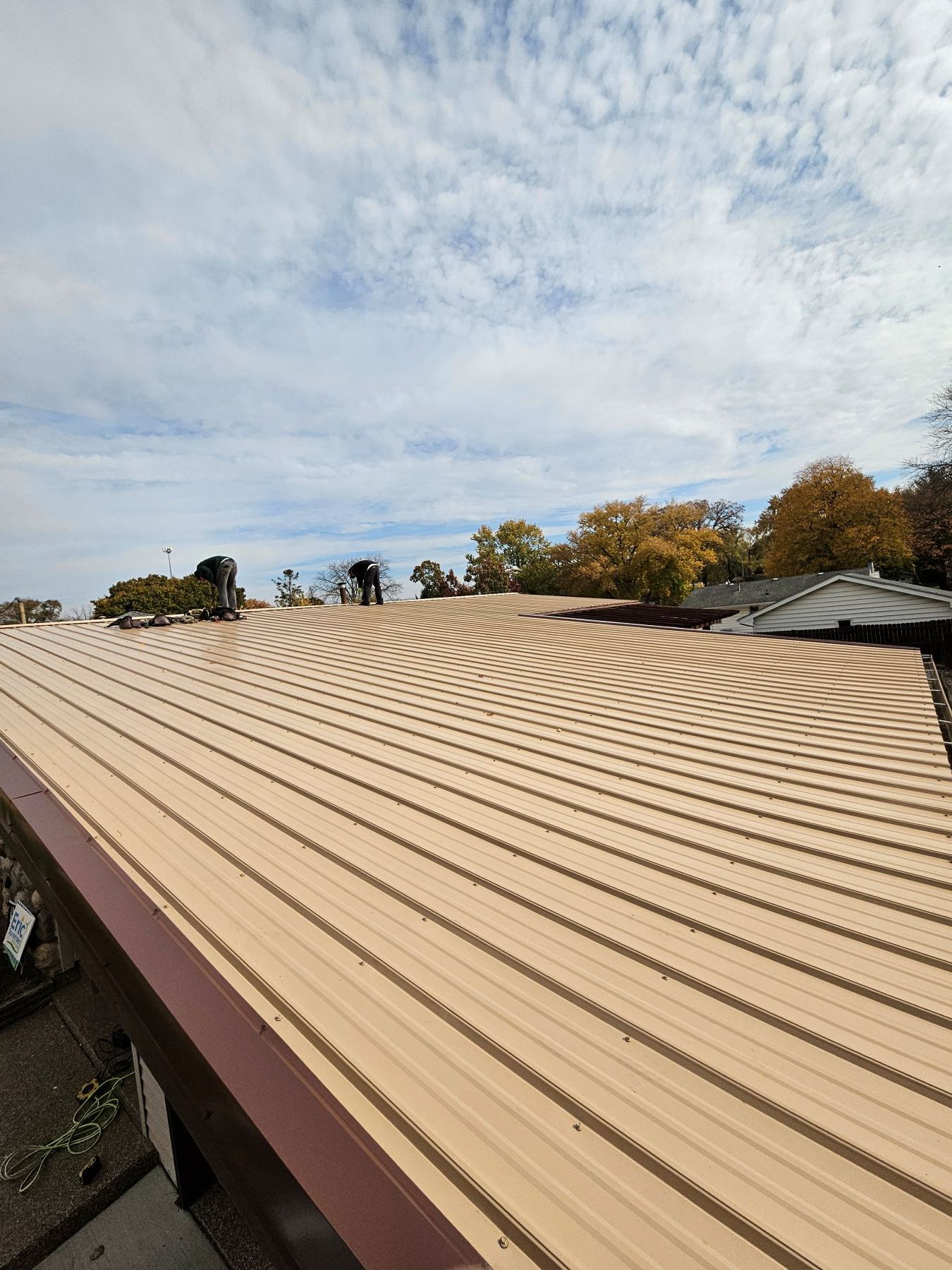 Tan corrugated metal roof with brown trim under a partly cloudy sky.