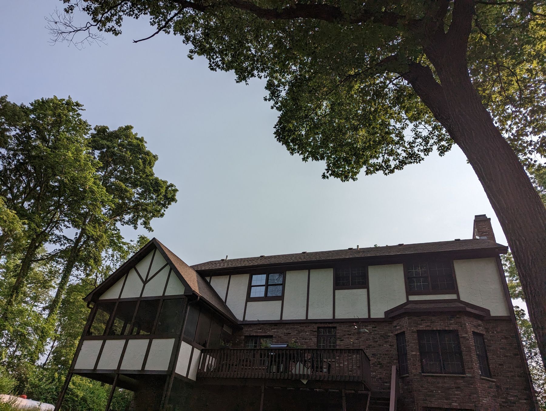 Two-story house with Tudor-style details, nestled amongst trees under a clear sky.