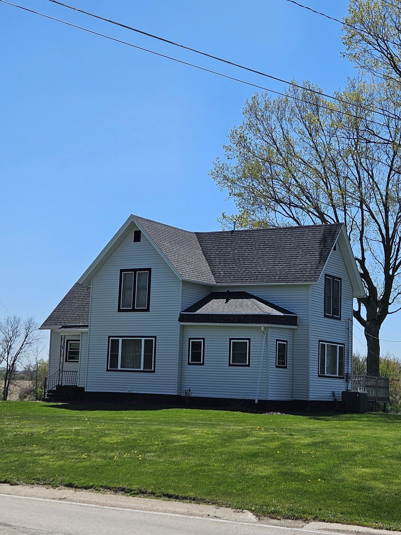 Two-story light blue house with black roof and windows against a blue sky, set on a green lawn.