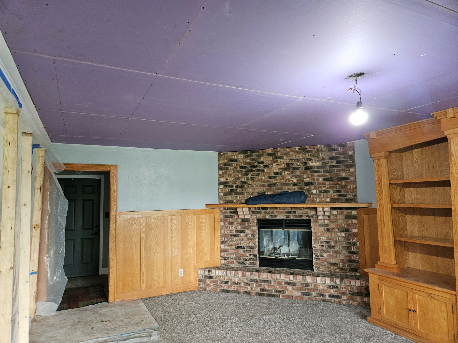 Renovated room with fireplace, bookshelves, and partially exposed walls. Purple ceiling, brick, and wood elements.