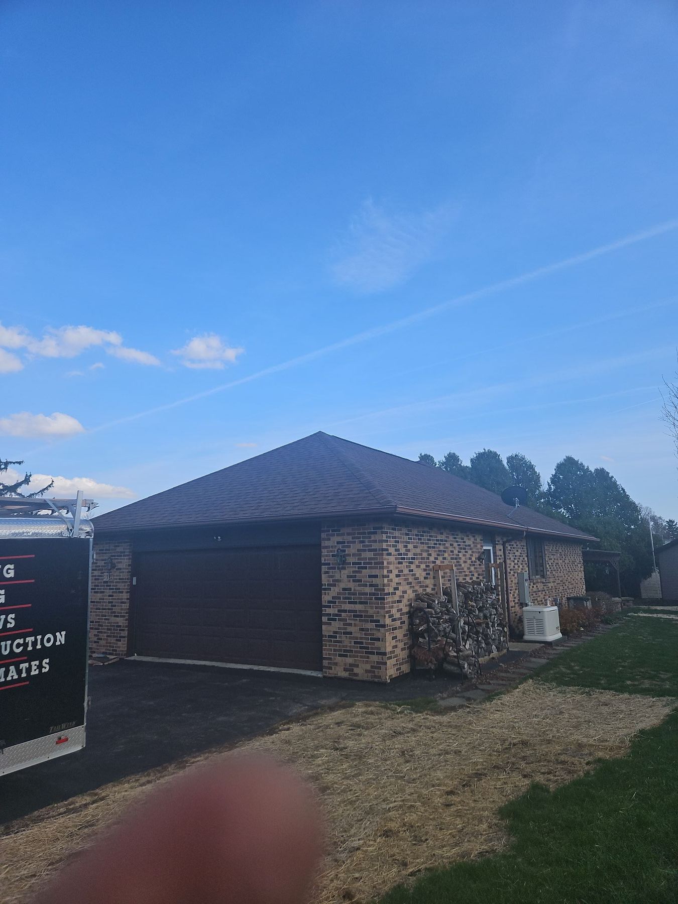 Brick house with brown garage door and roof under a blue sky.