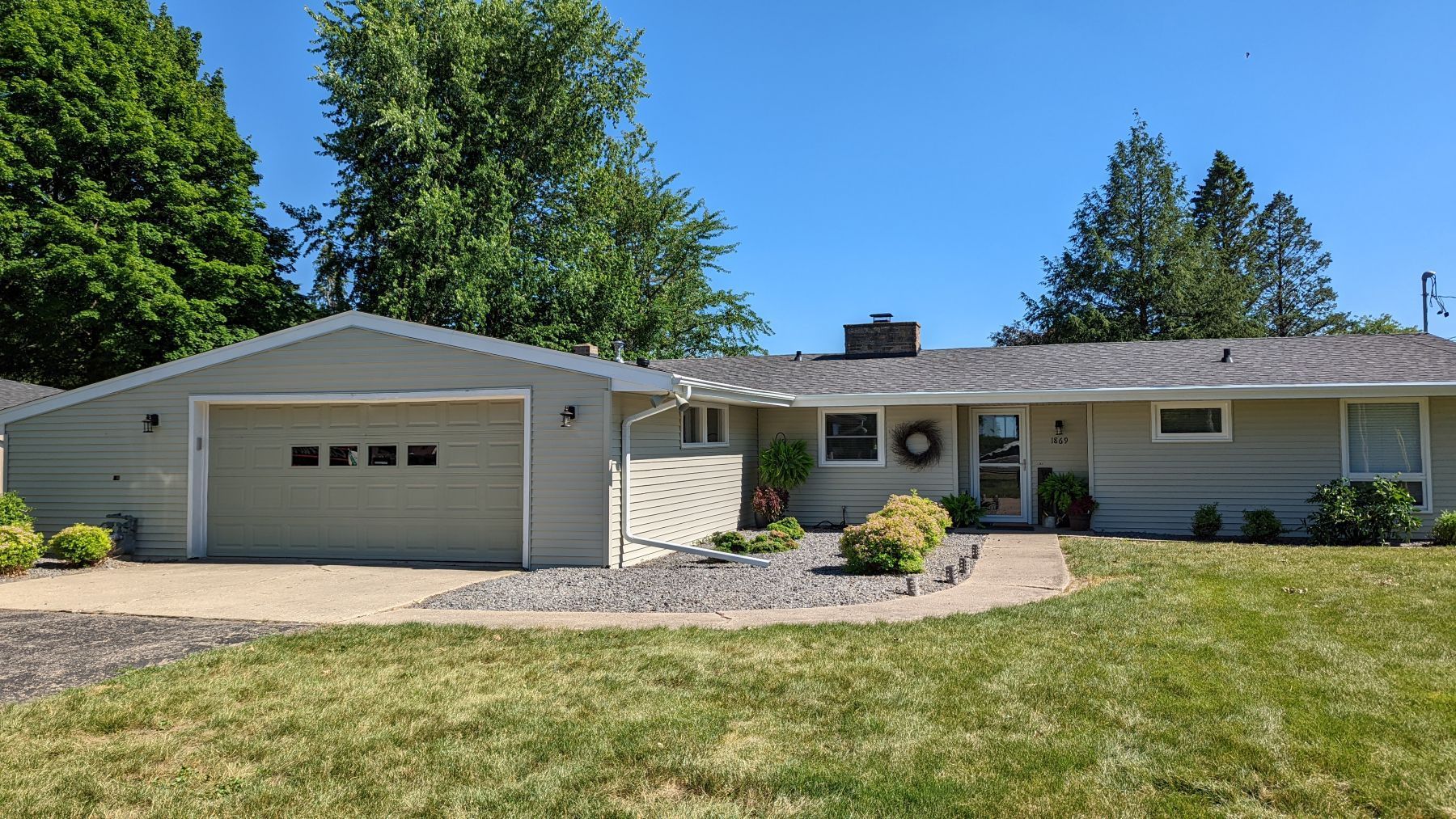 A single-story beige house with a garage and green lawn under a blue sky.
