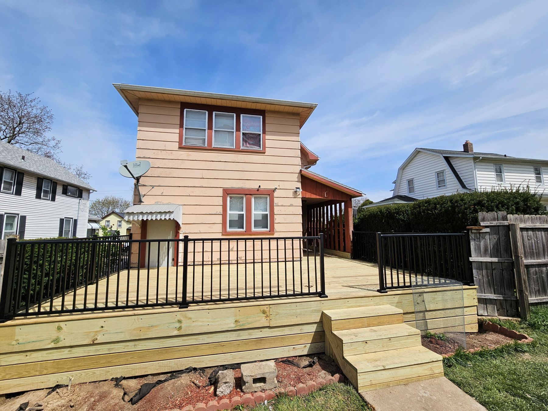 Back of a two-story house with a wooden deck and black railings. Cloudy blue sky.